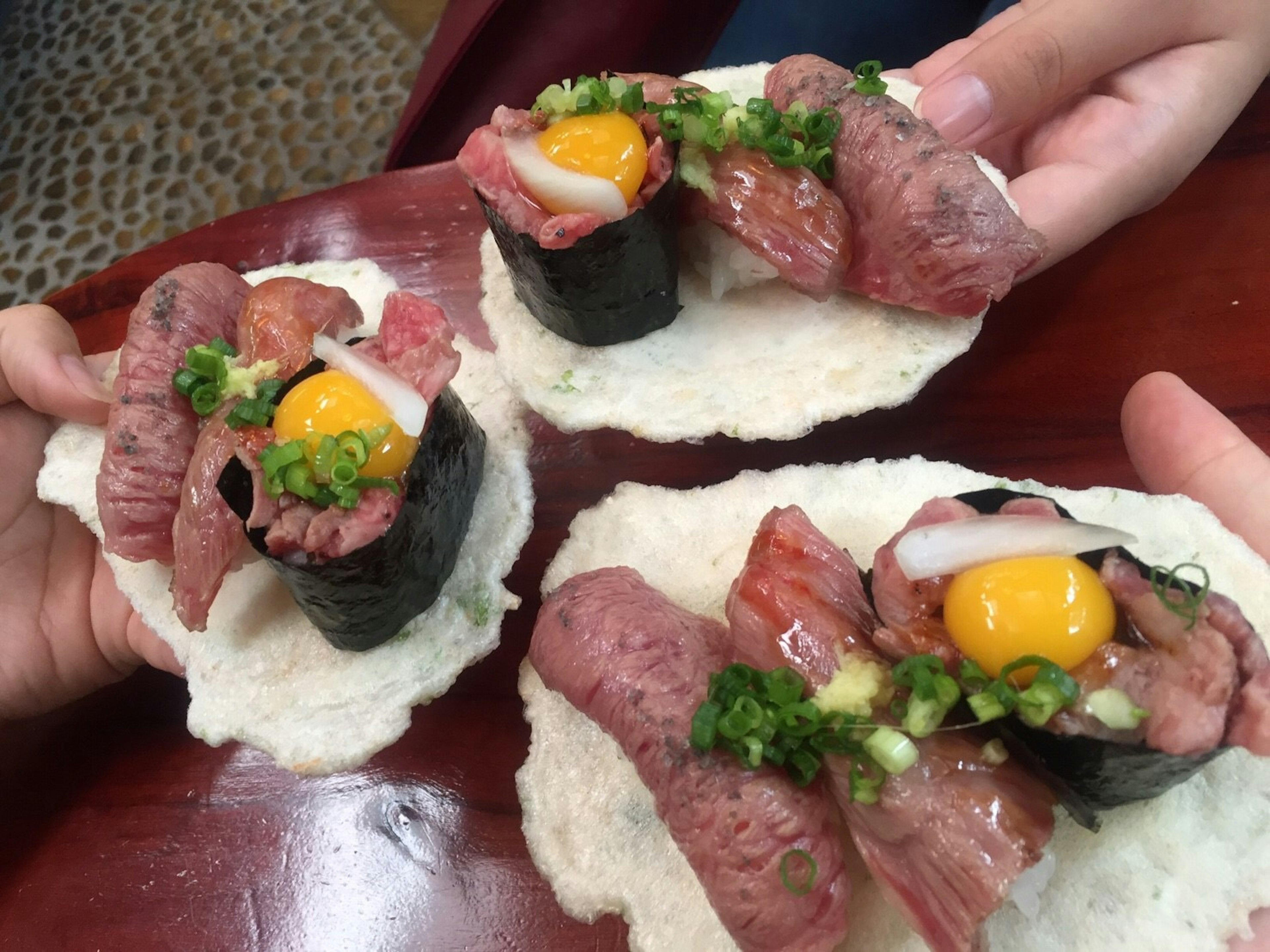 Sushi topped with egg yolk and green onions on a rice cracker served in hands