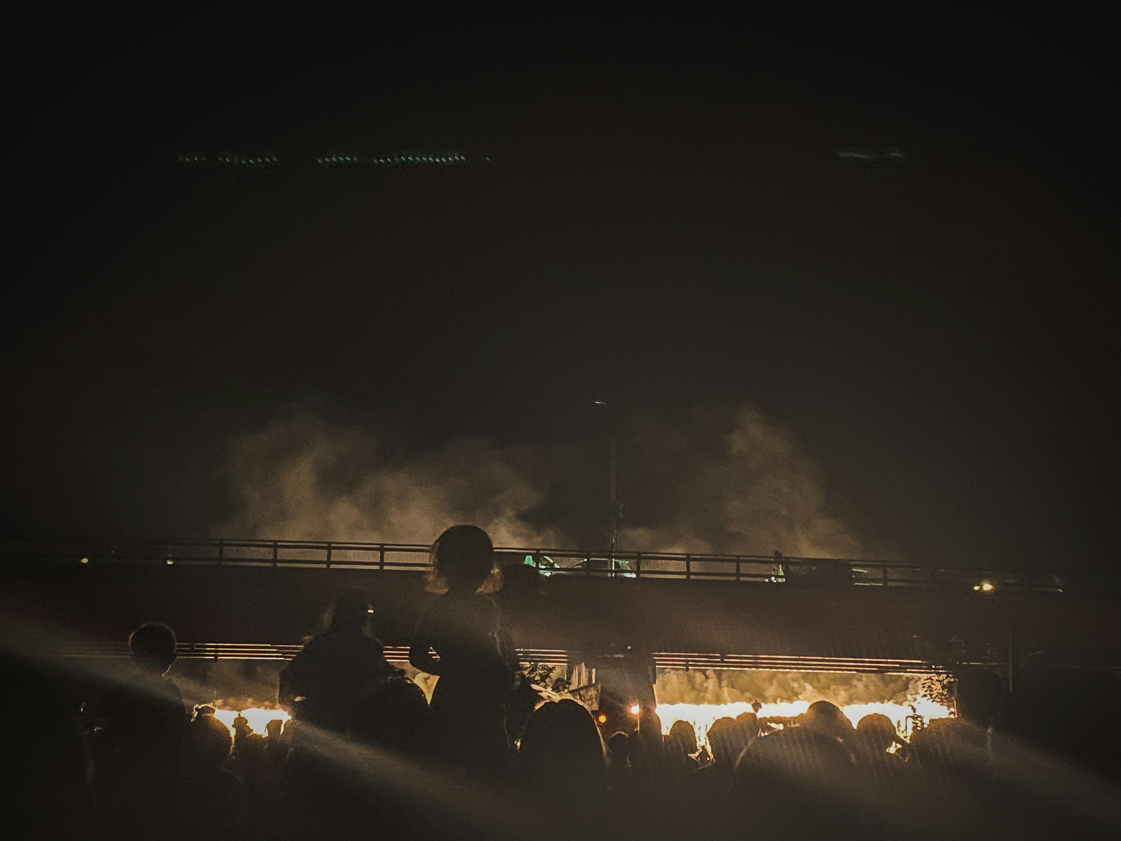 Silhouette of a crowd against smoke and flames at night