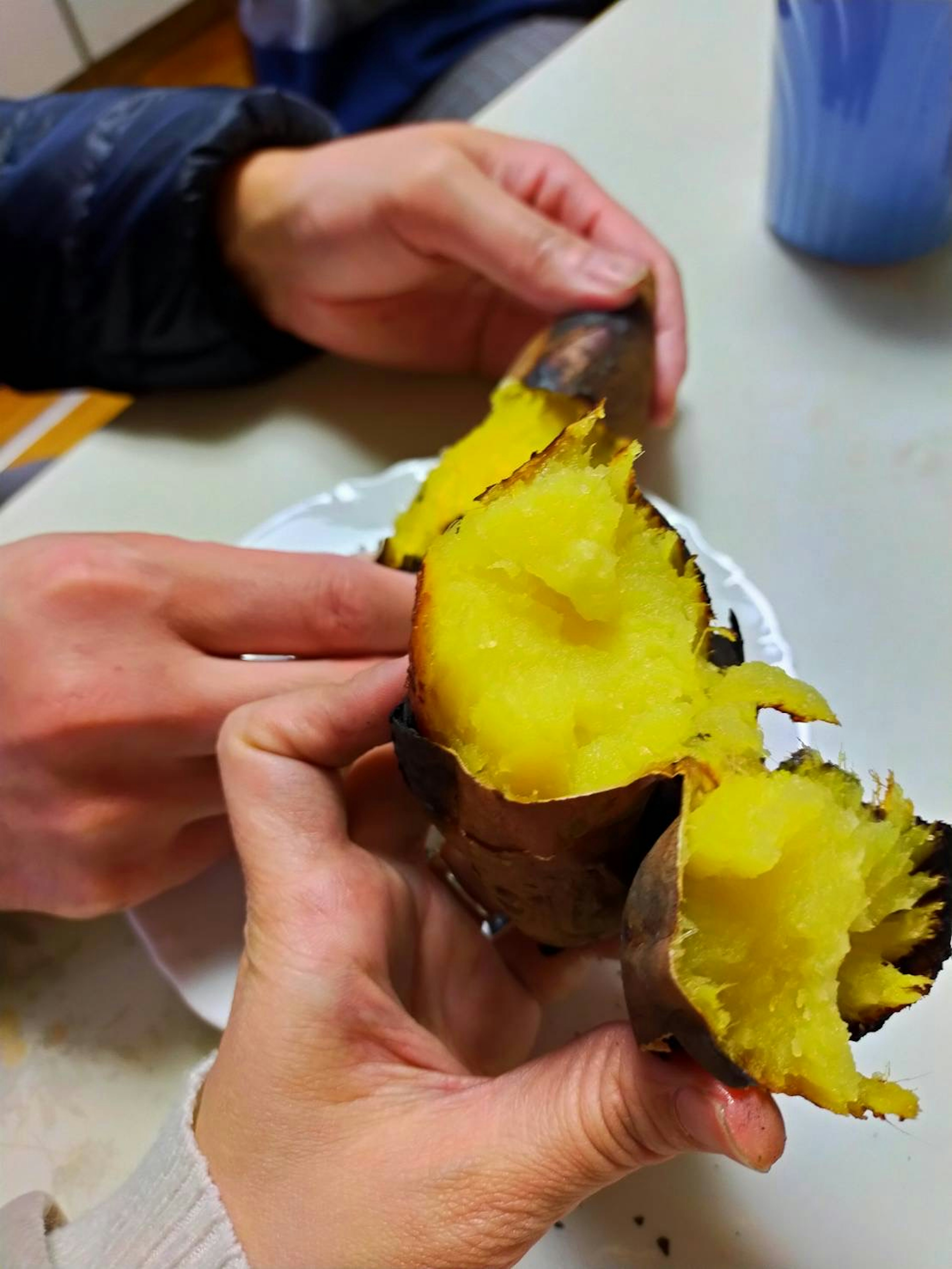 Zwei Hände halten eine gebackene Süßkartoffel, die ihr gelbes Fleisch zeigt