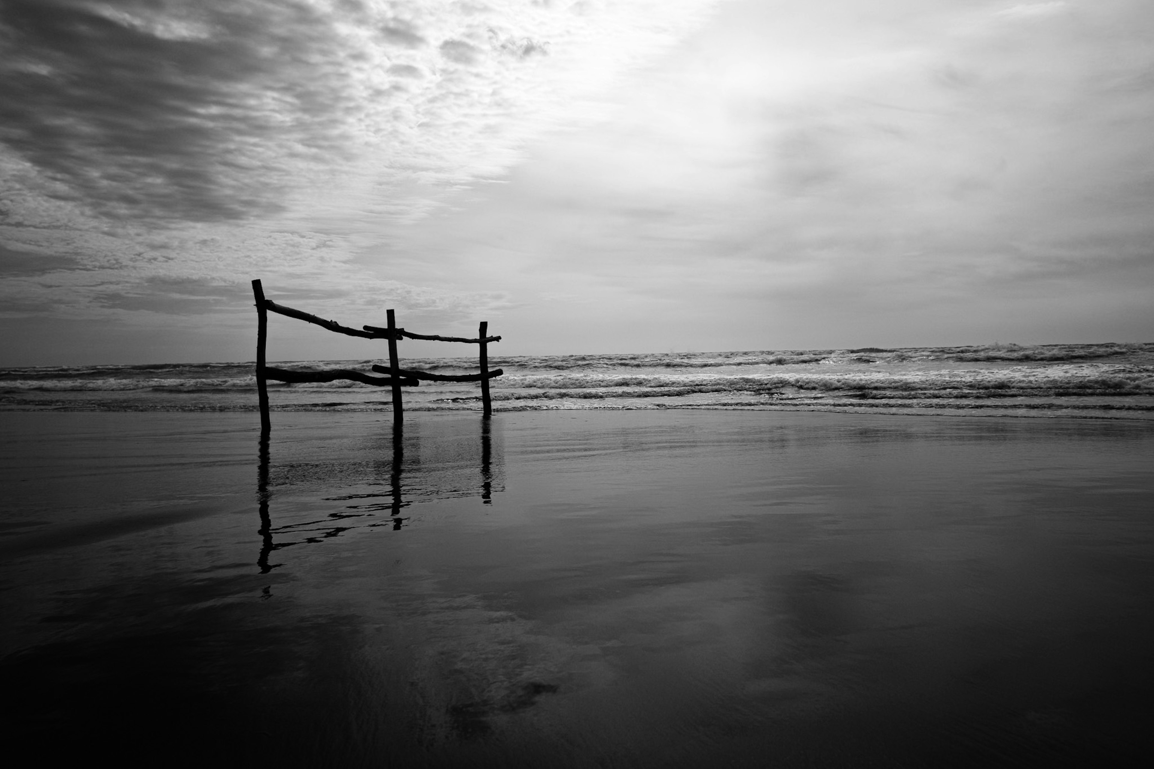 Cerca de madera en una playa en blanco y negro con olas tranquilas