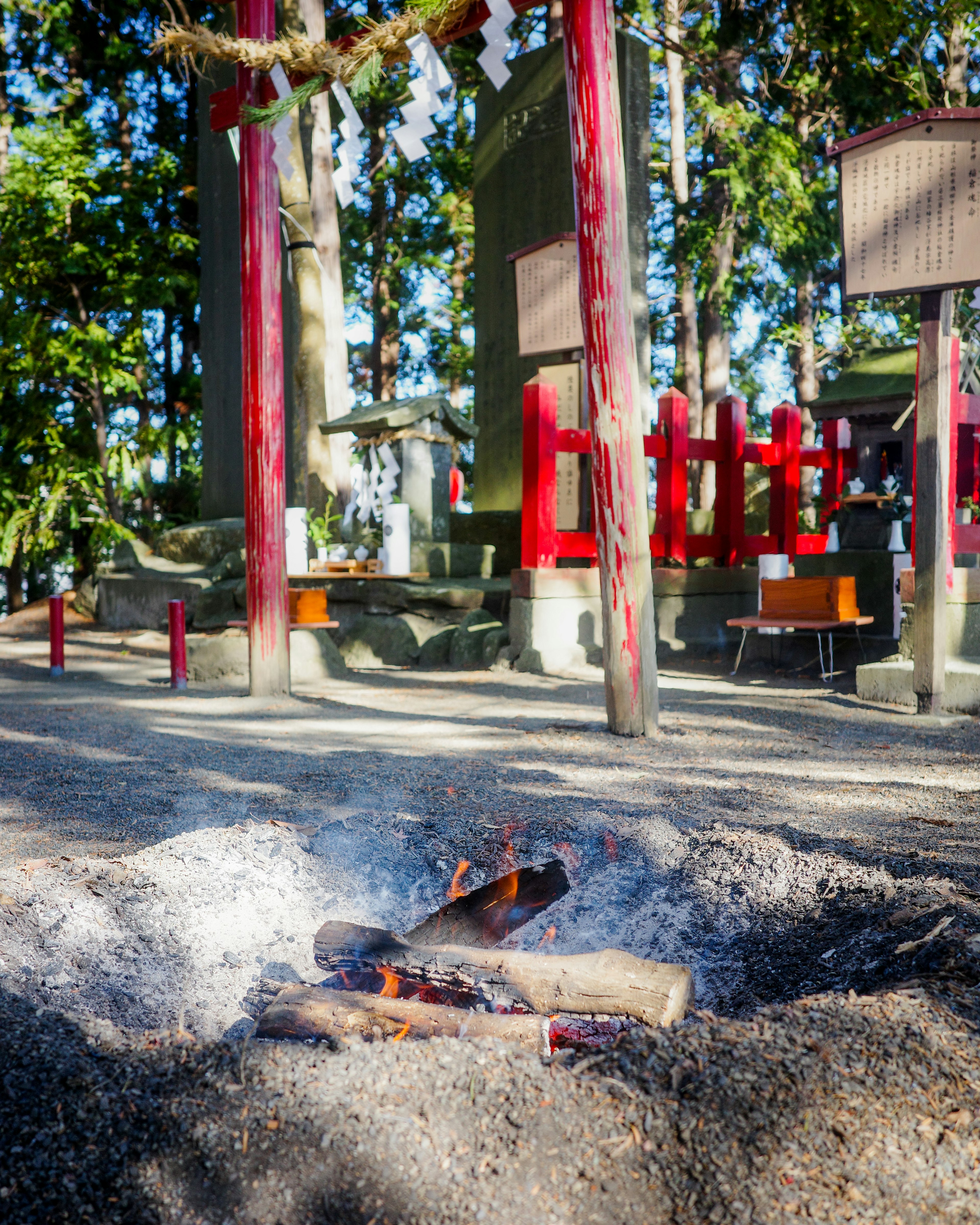 A scenic view featuring a shrine with red pillars and a fire pit surrounded by ash