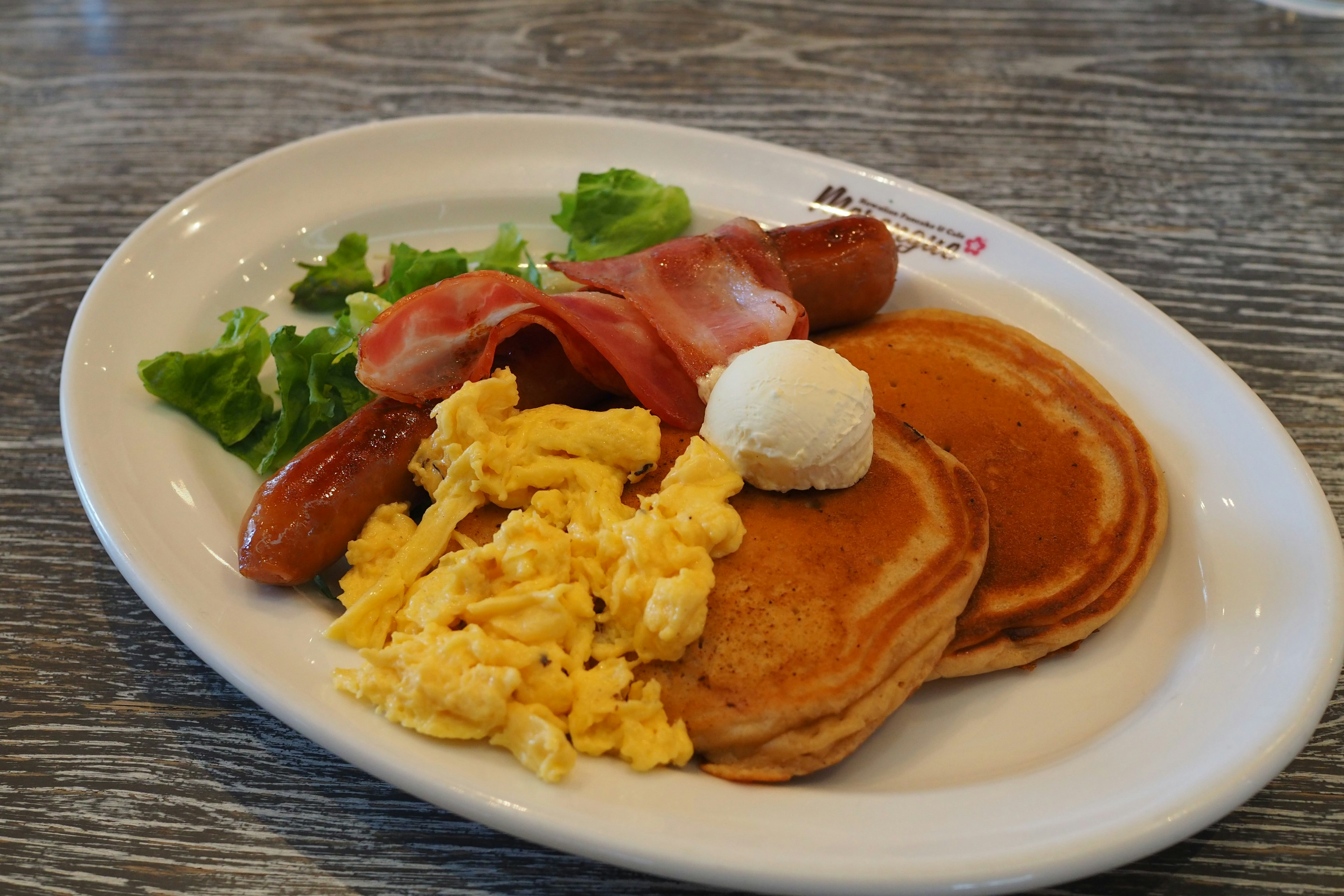 Breakfast plate with pancakes scrambled eggs bacon sausage lettuce and butter