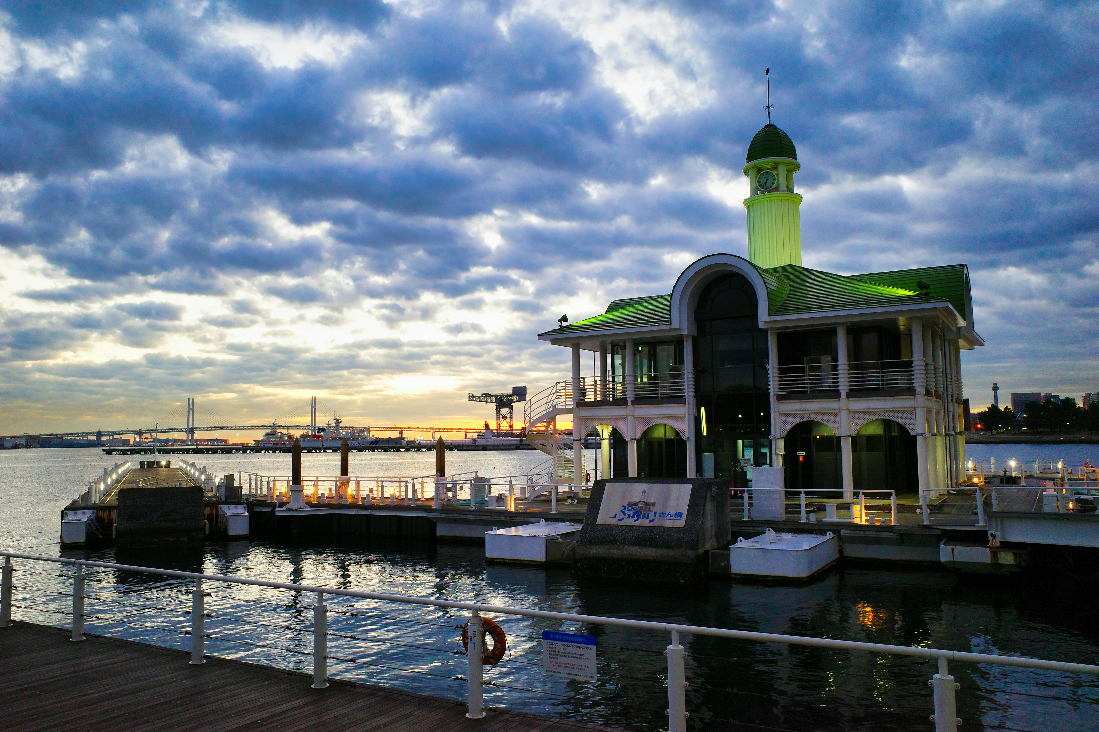 A waterfront building with a green roof at sunset surrounded by clouds