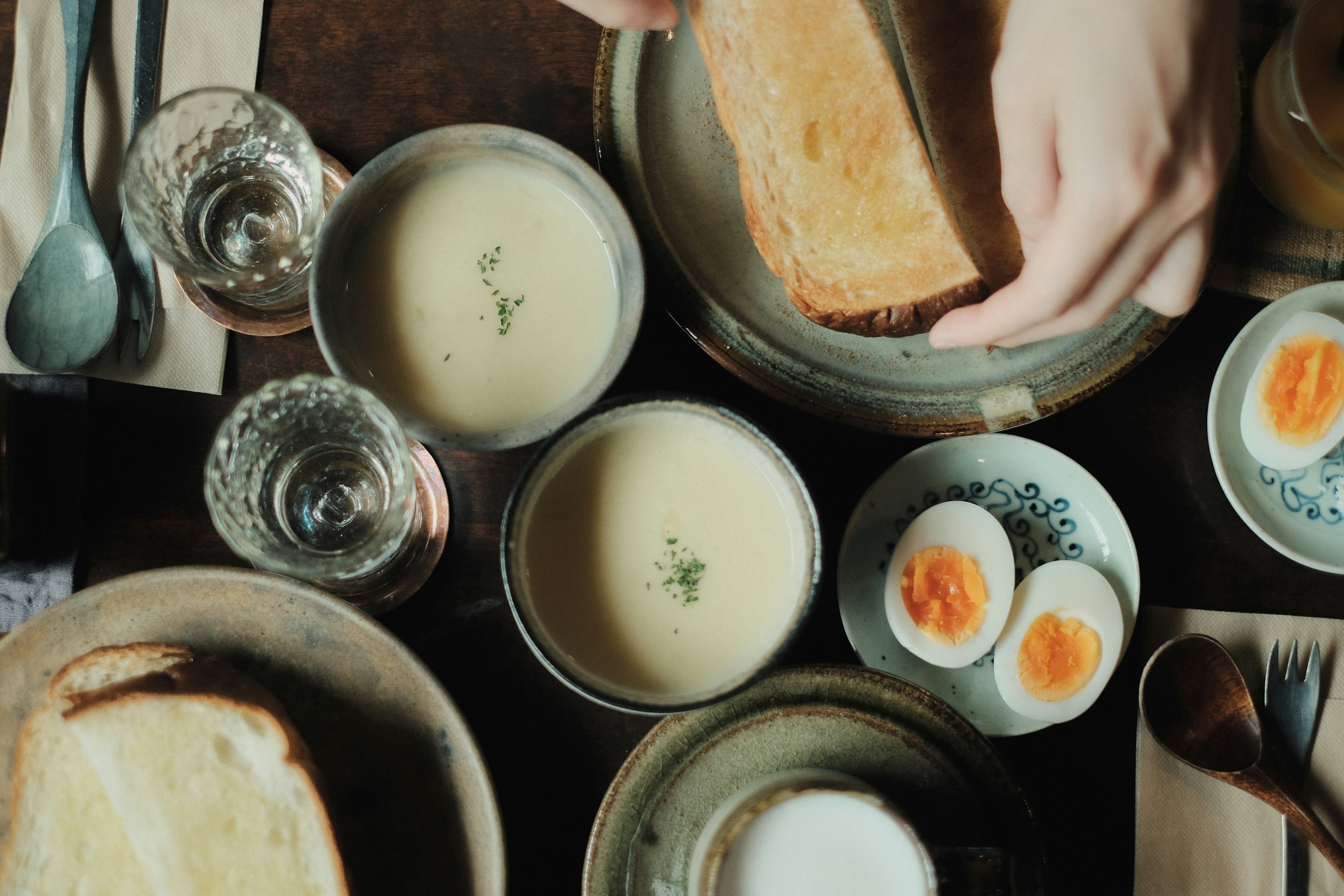 Breakfast scene on a table featuring toast soup boiled eggs and glasses