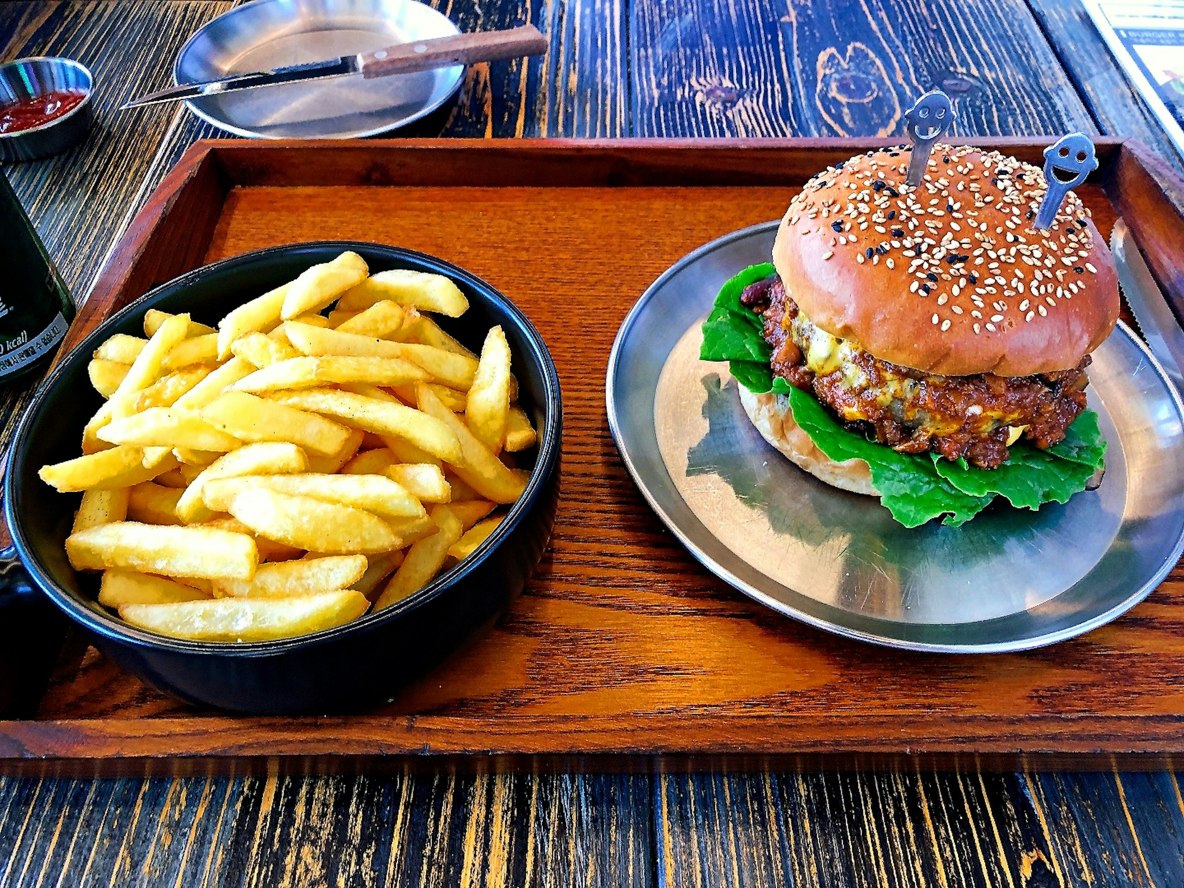 Ein Burger mit Sesambrötchen und Pommes auf einem Holztablett