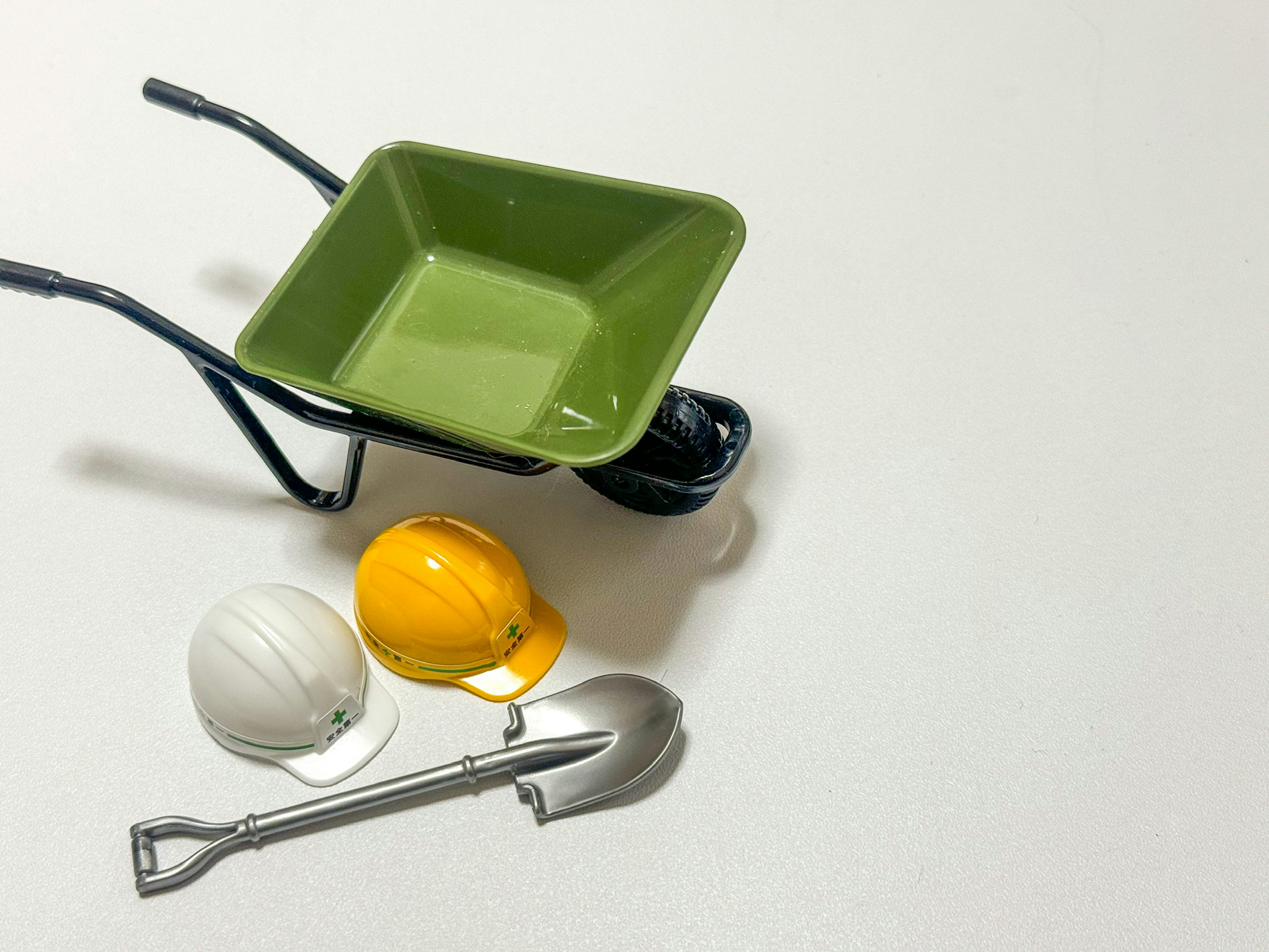 A green wheelbarrow with construction helmets and a shovel on a work surface