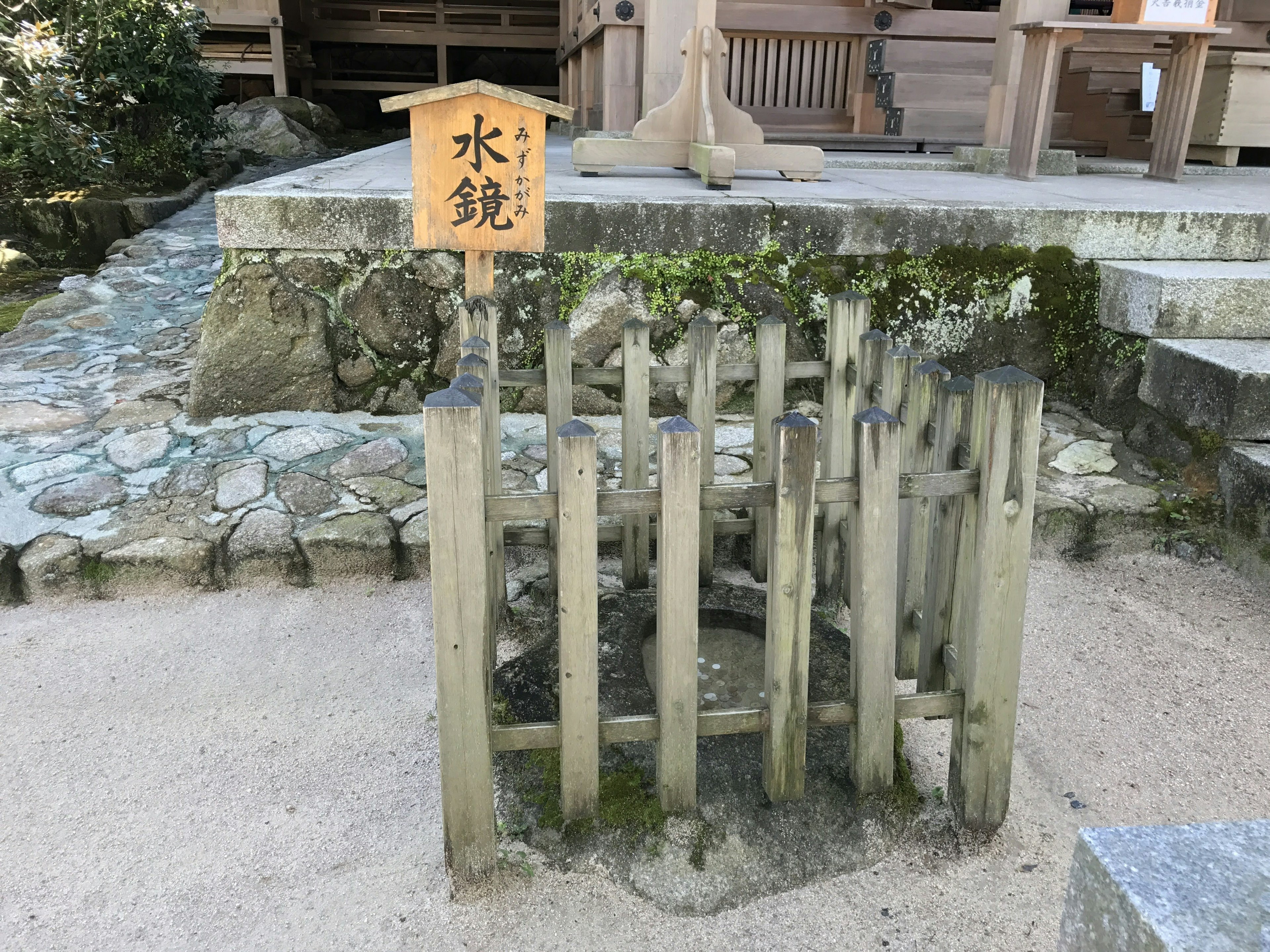 水鏡の看板がある木製の囲いと石の道の風景