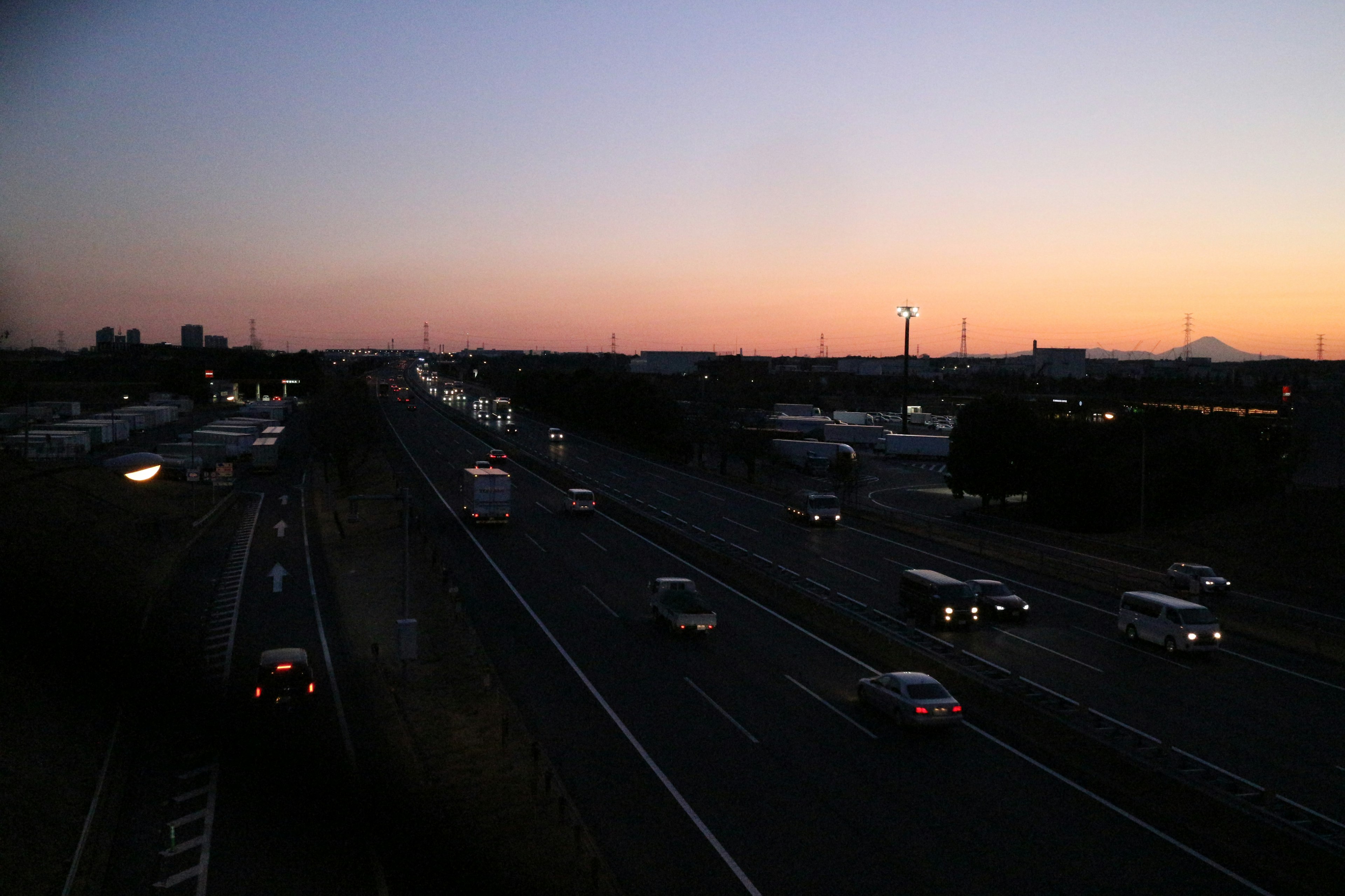 Vista crepuscolare di un'autostrada con luci di auto illuminate e turbine eoliche visibili