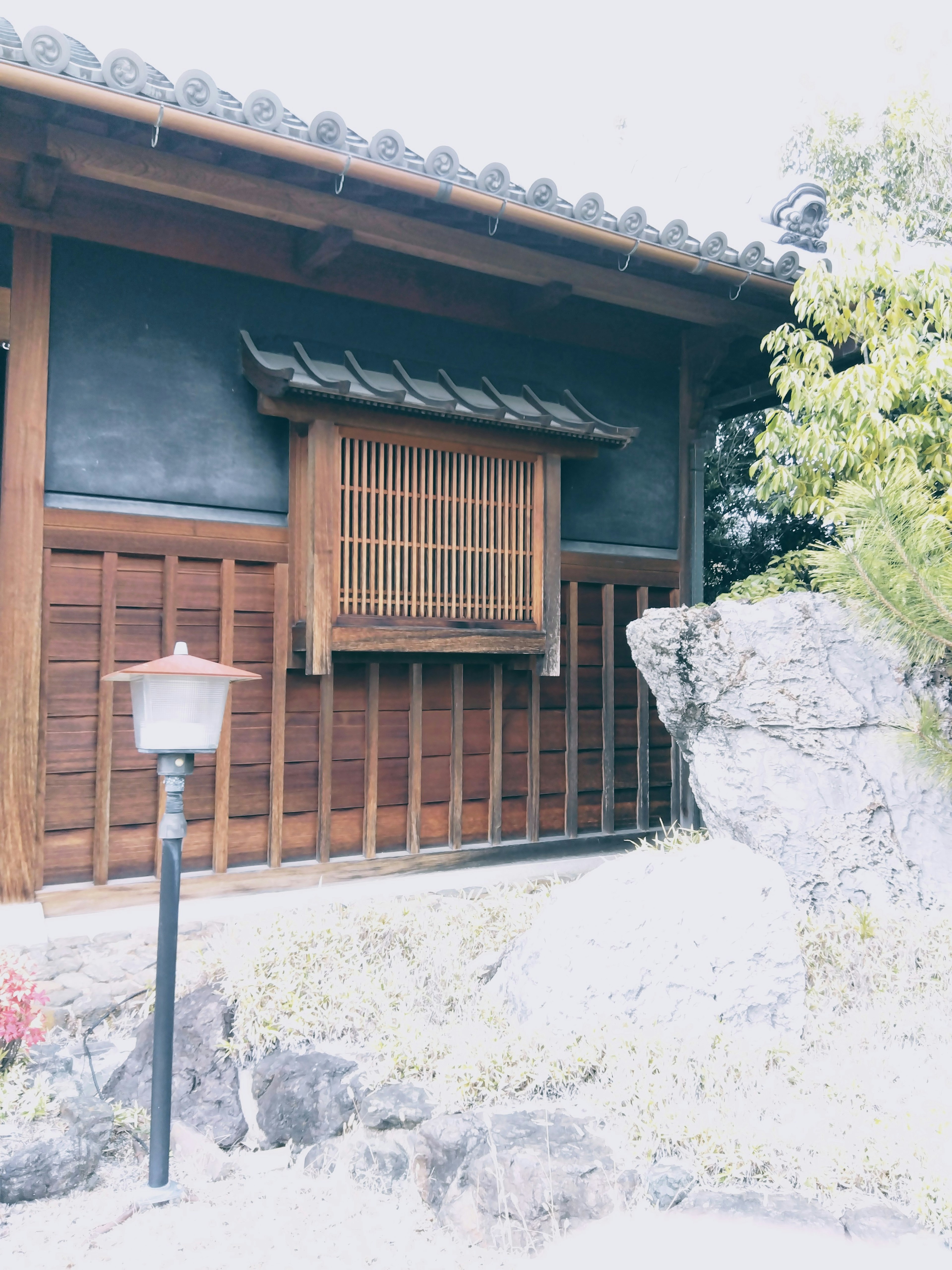 Außenansicht eines traditionellen japanischen Hauses mit Holzdesign Steinelementen und Fenstergitter mit Grünpflanzen