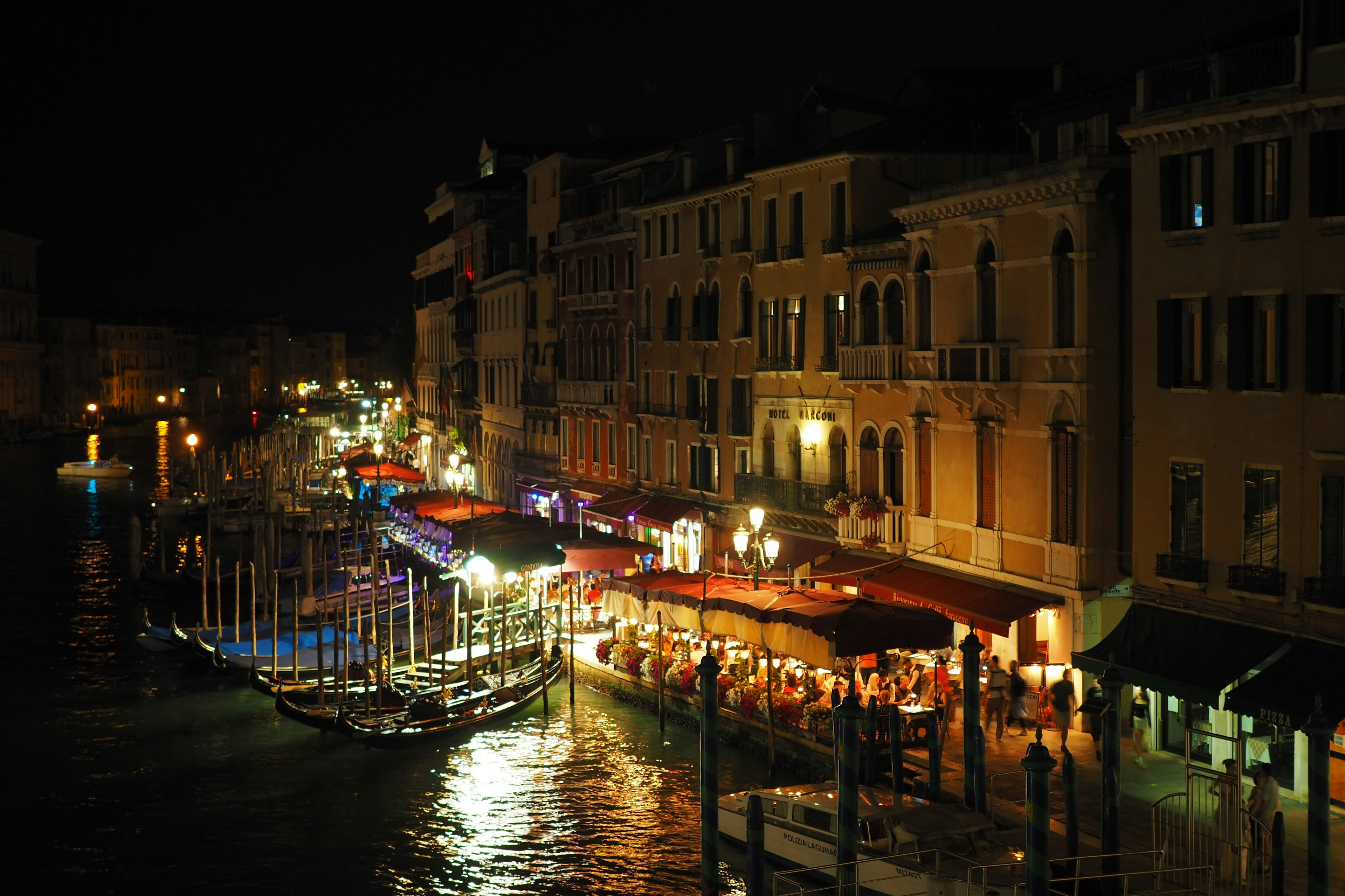 Vista nocturna de Venecia con restaurantes iluminados y barcos a lo largo del canal