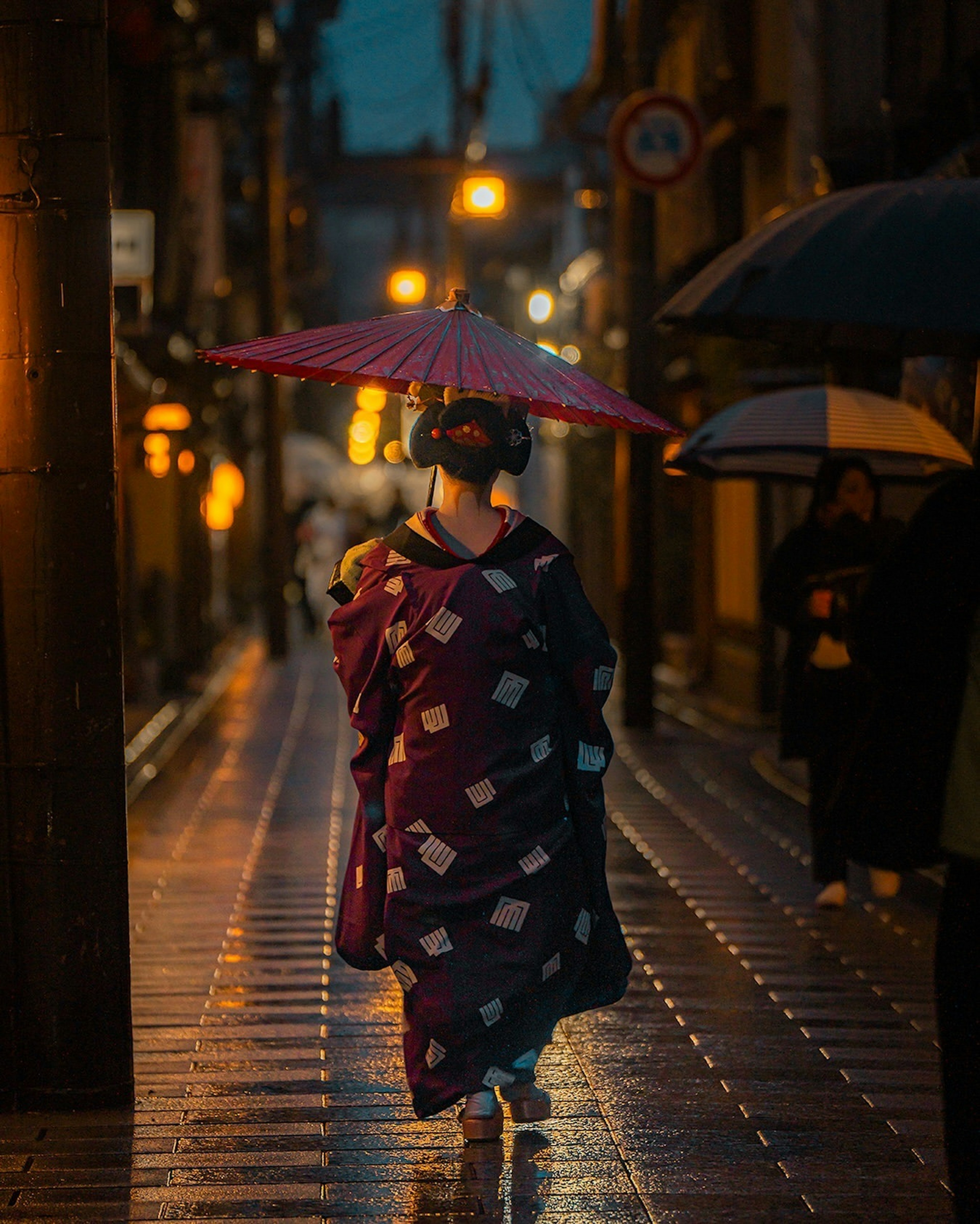 Donna in kimono che cammina per strada di notte con un ombrello