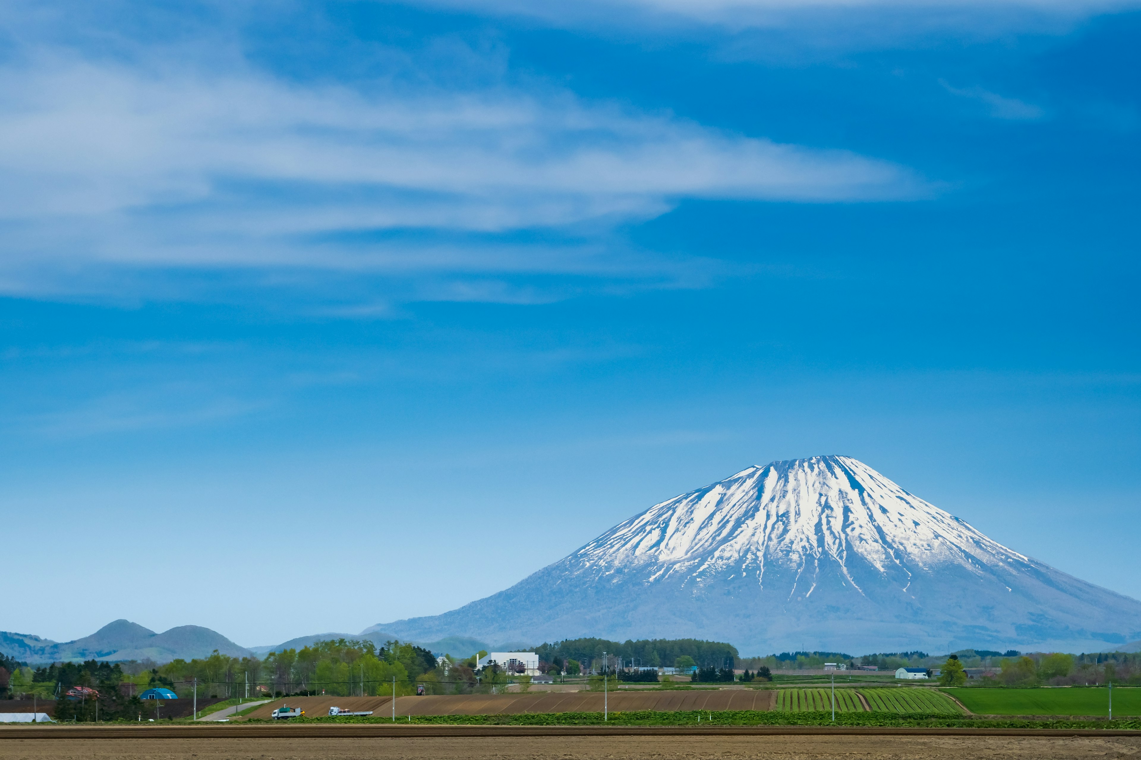 Vue panoramique d'une montagne enneigée sous un ciel bleu avec des champs et des villages