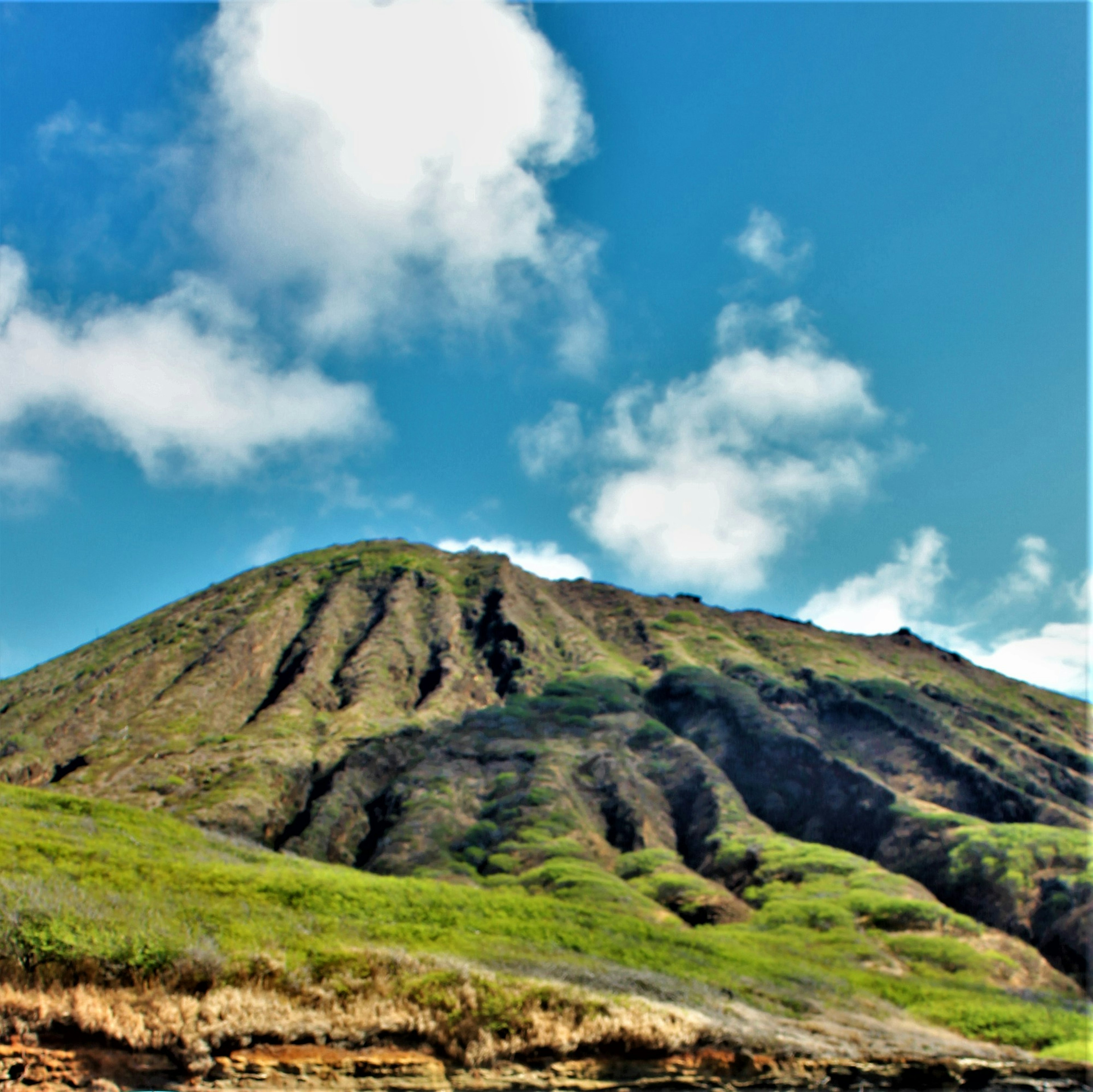 Paisaje de una montaña verde bajo un cielo azul con nubes blancas