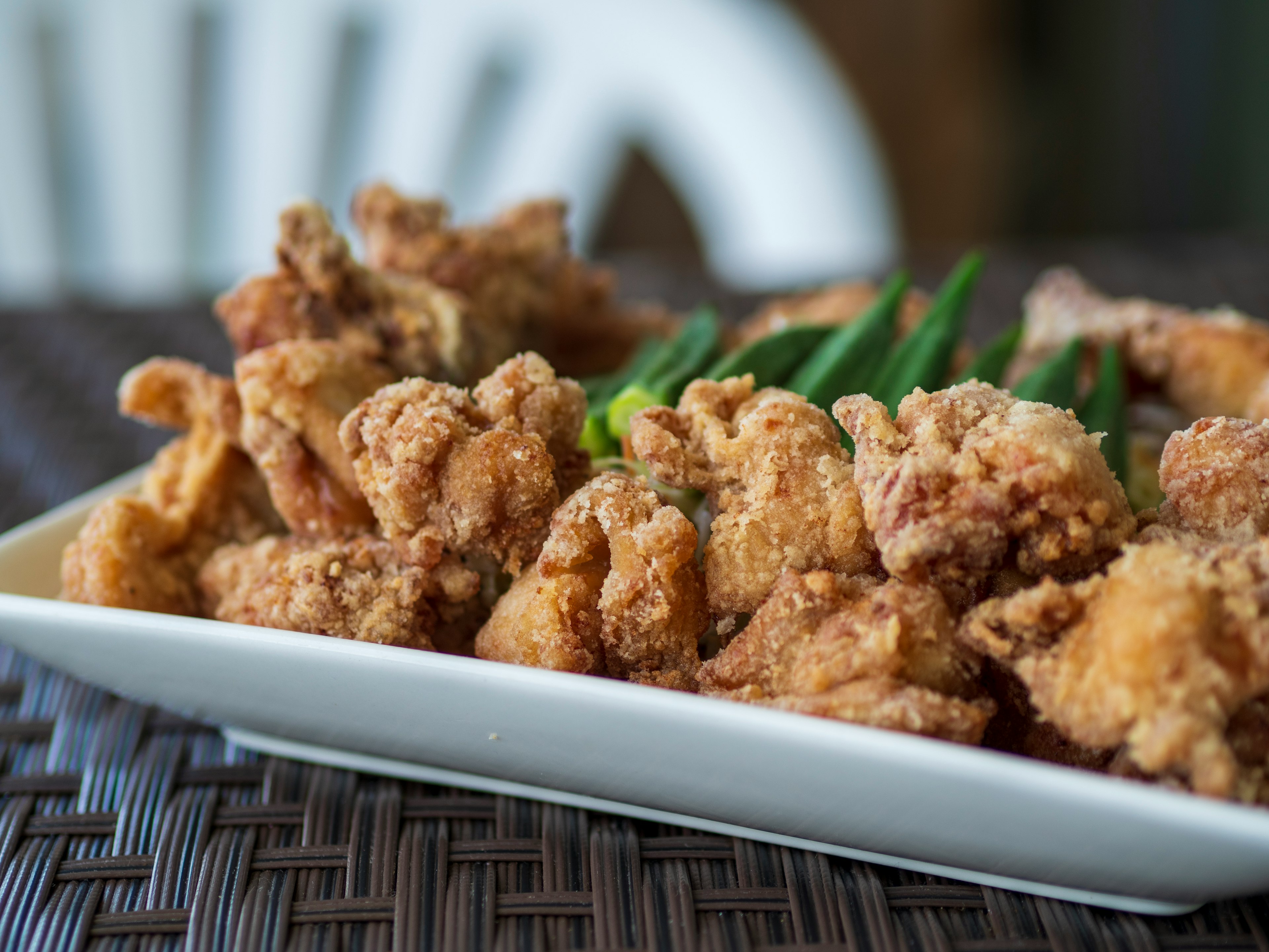 Crispy fried chicken served on a white plate with fresh okra