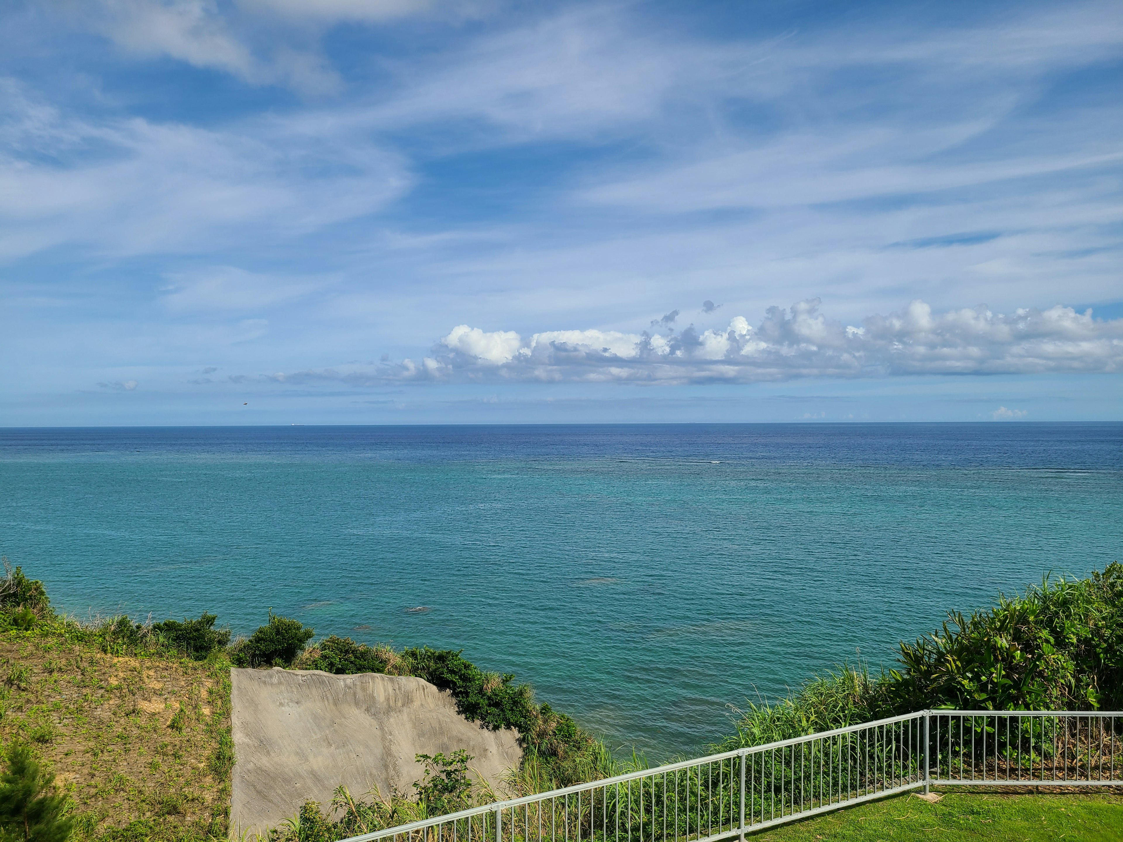 Malersicher Blick auf den blauen Ozean und den Himmel mit grünen Hügeln und einem weißen Zaun