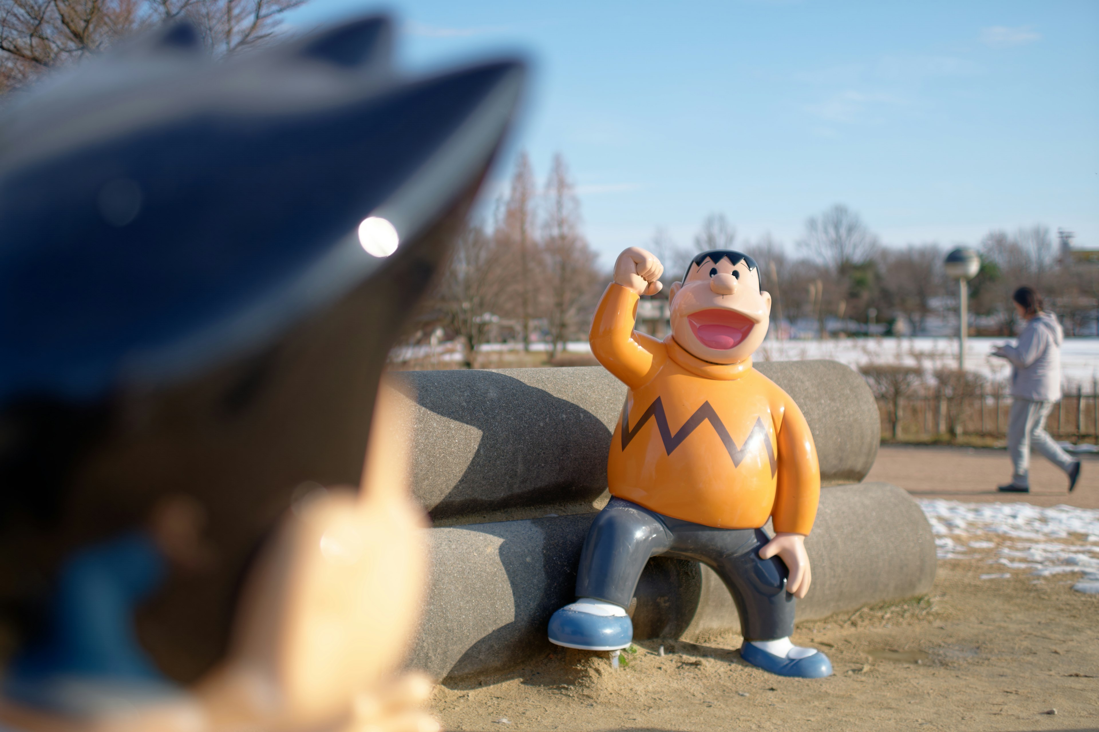 Figurita de Crayon Shin-chan sentada en un parque con una persona al fondo