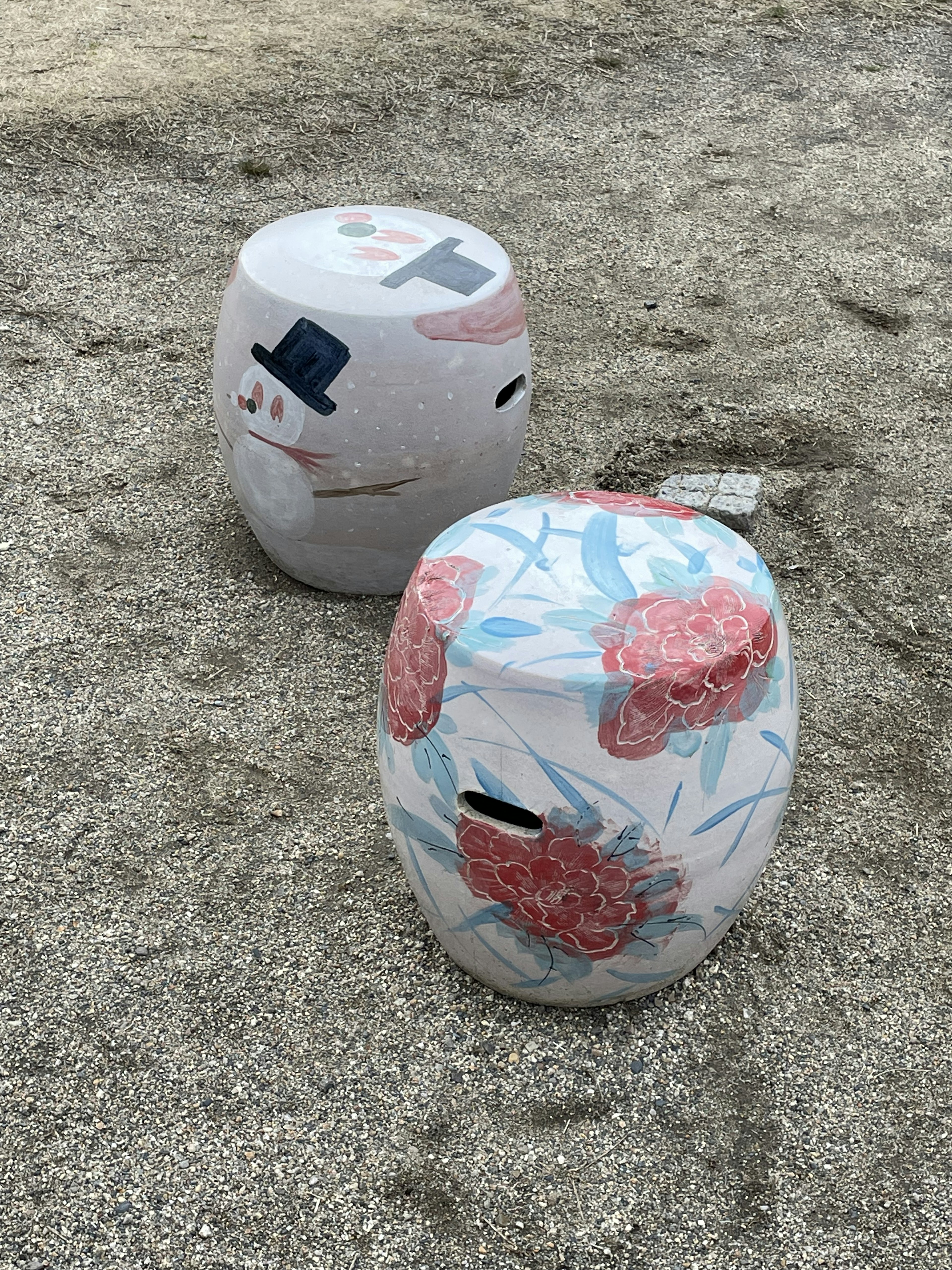 Two decorative objects one resembling a snowman and the other with floral patterns placed on sandy ground