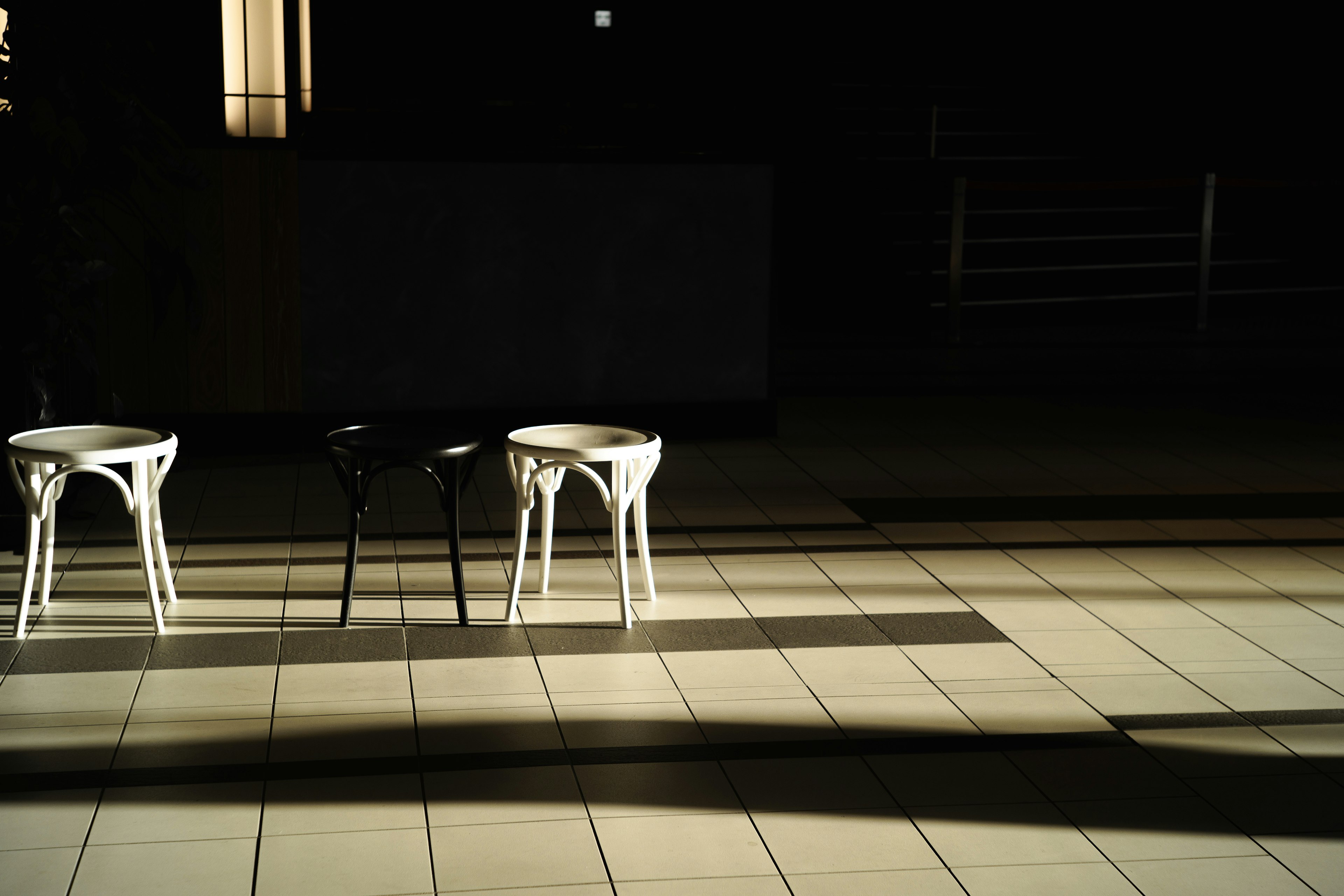 Three chairs in white and black casting shadows on tiled floor