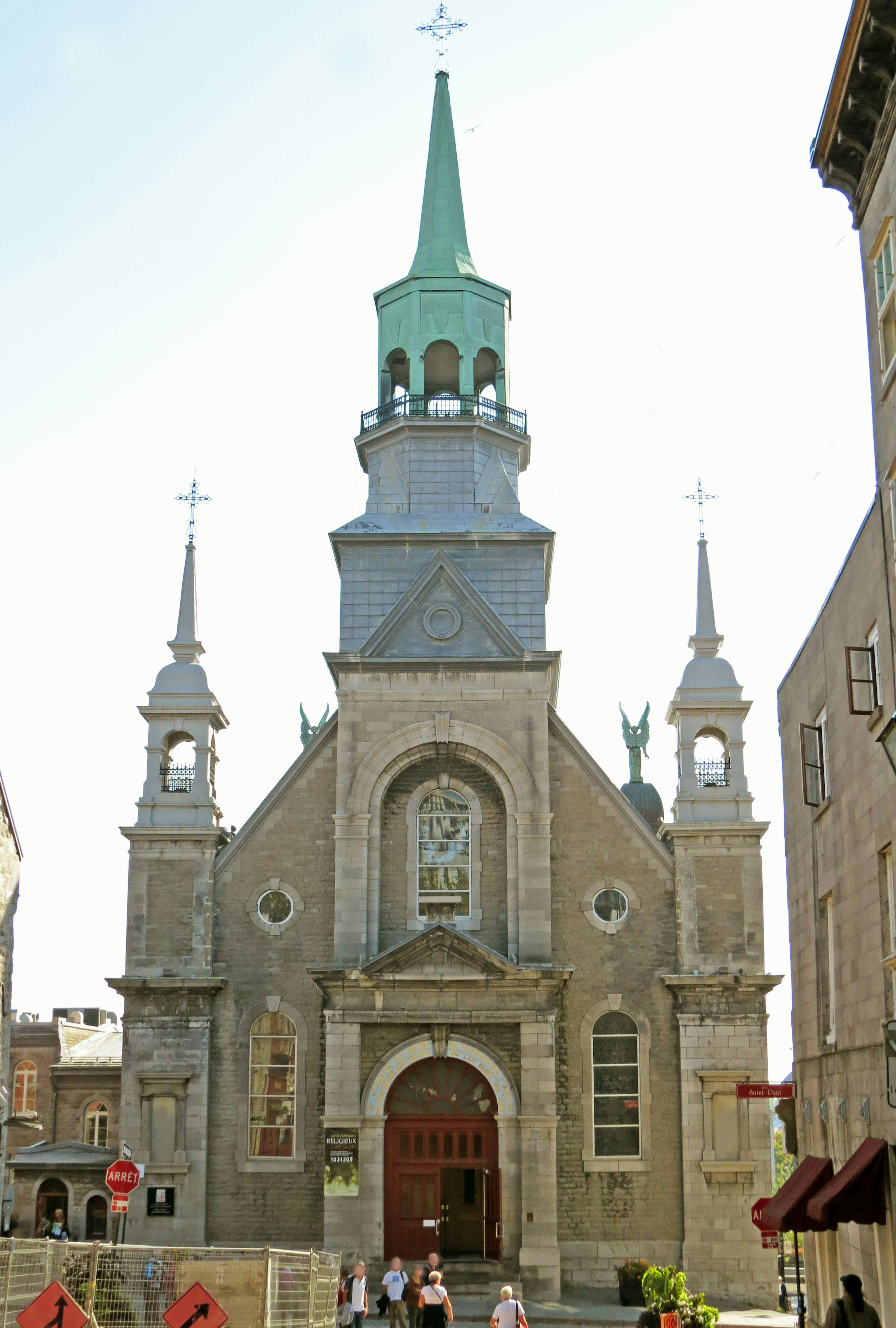 Façade d'une église historique avec des flèches vertes entourant des bâtiments et des piétons