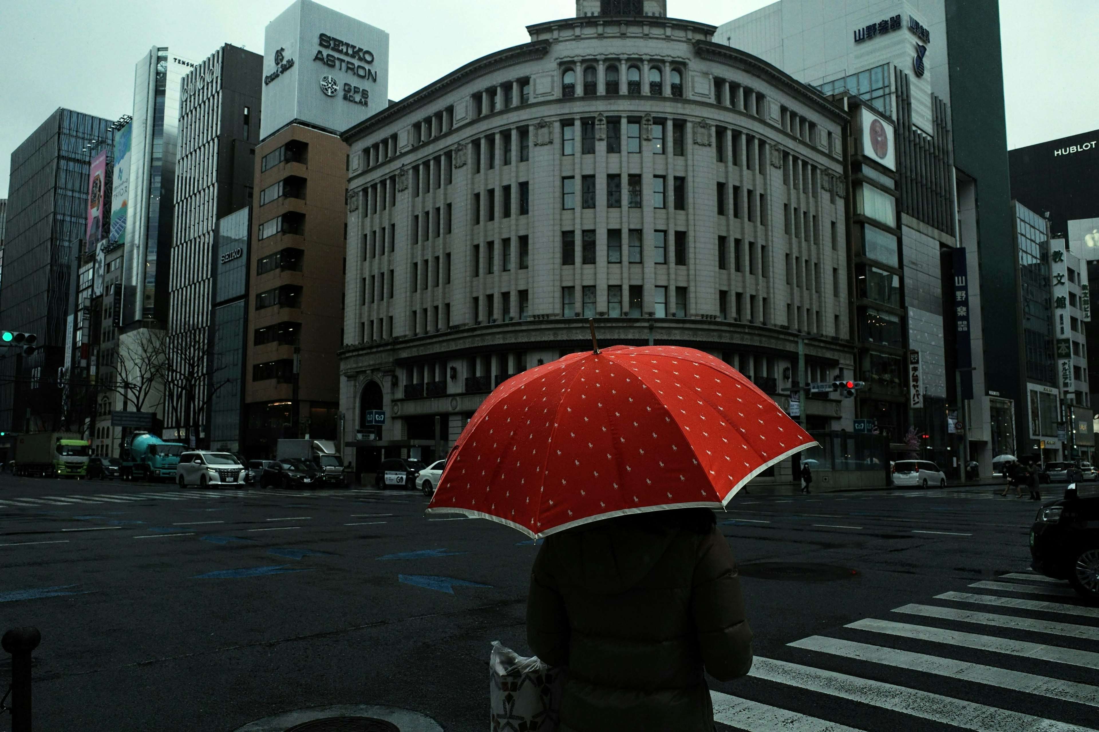 Una persona con un ombrello rosso si trova all'angolo di una strada con un edificio sullo sfondo