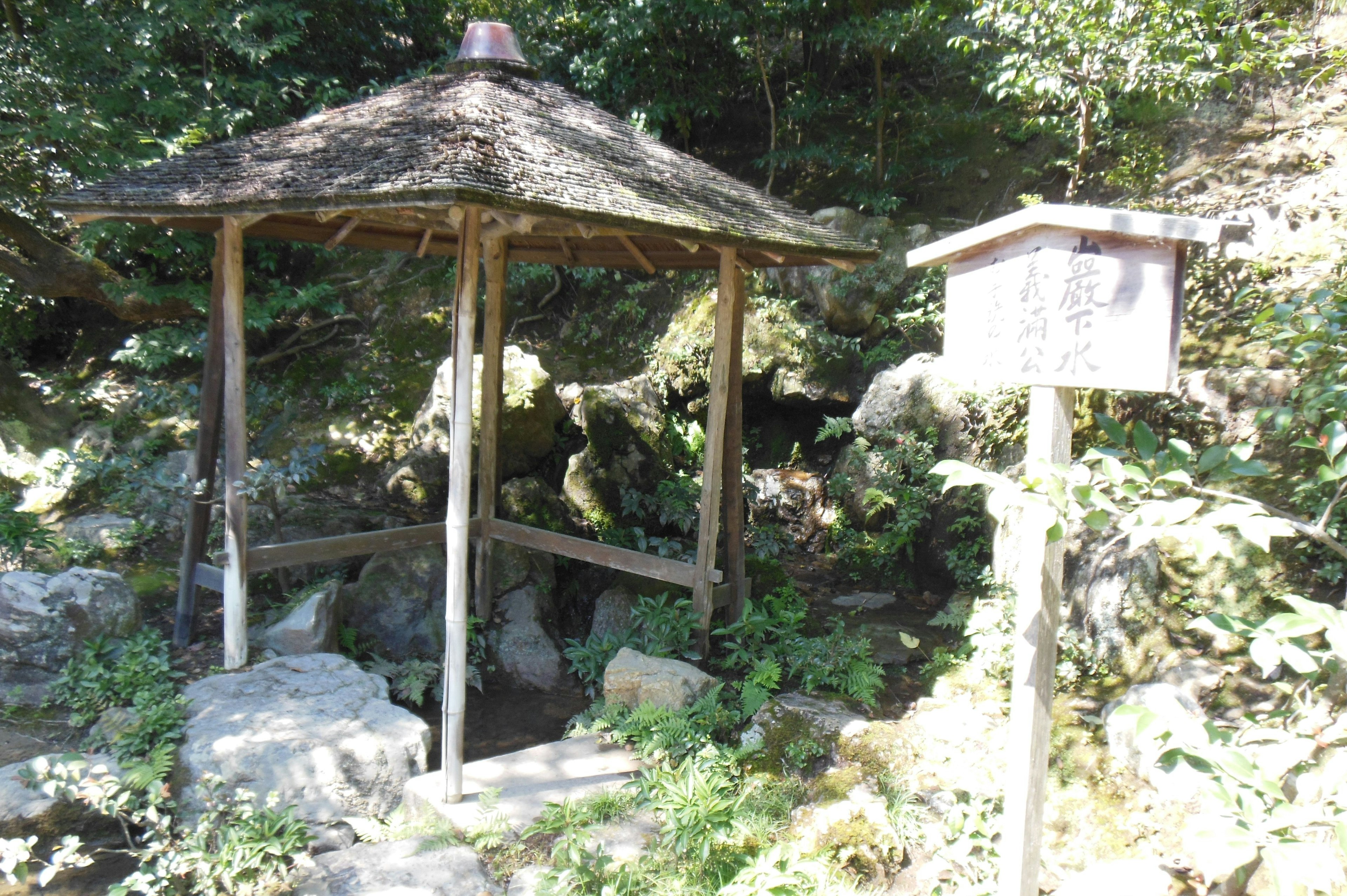 Wooden gazebo amidst lush greenery with a sign nearby