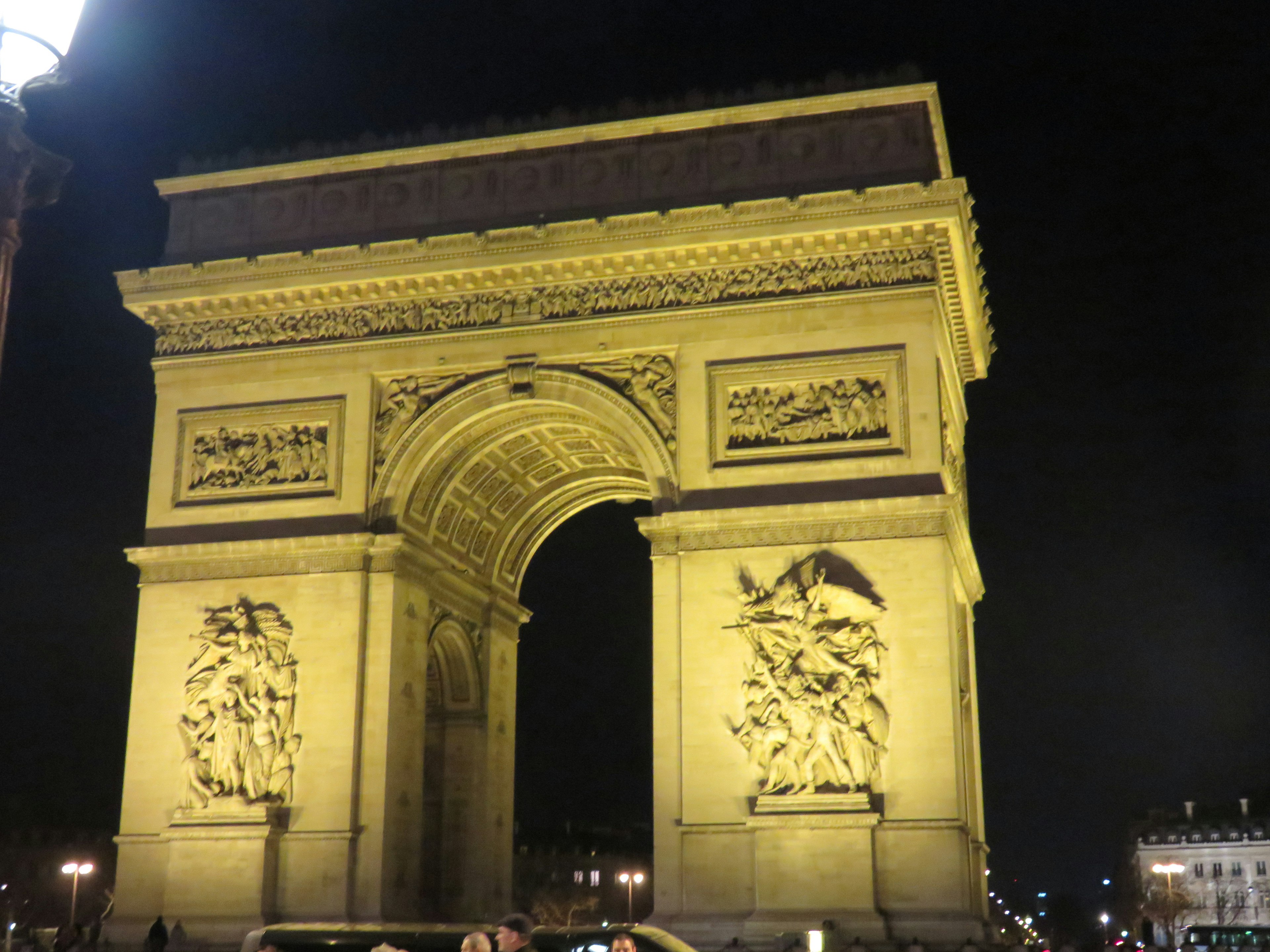 Arc de Triomphe yang diterangi di malam hari menampilkan lengkungan besar dan patung