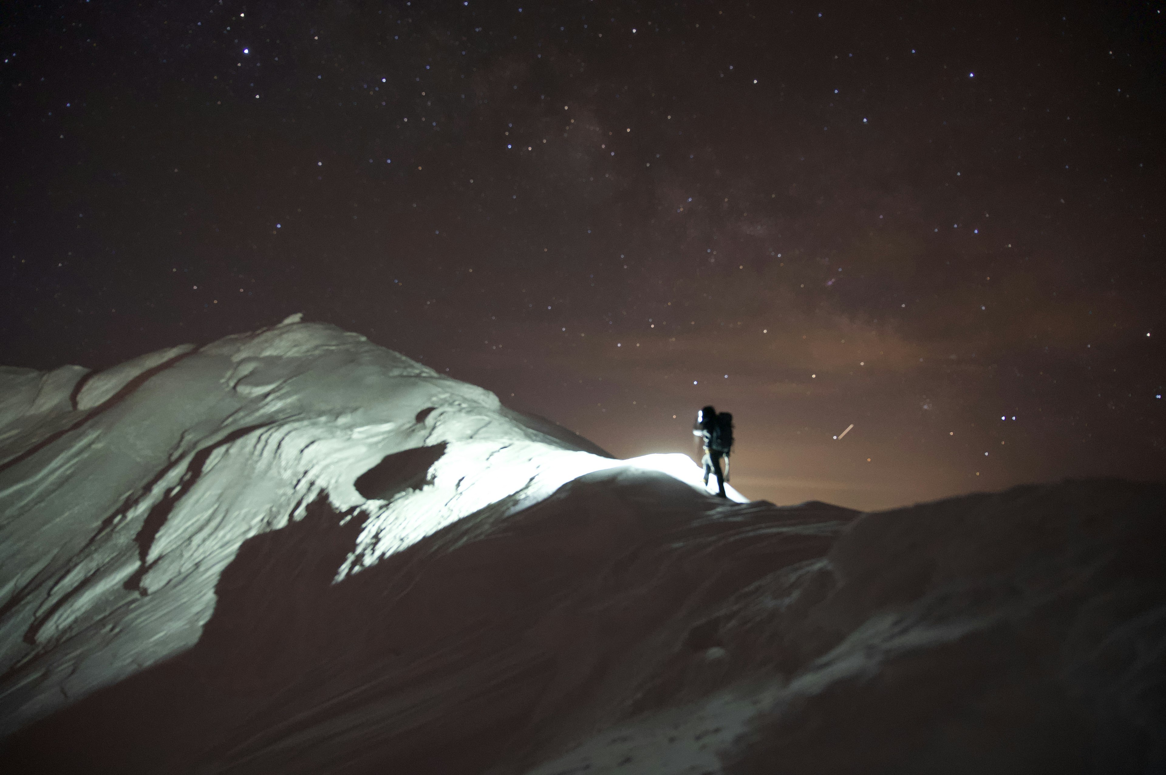 Silhouette di un alpinista su una montagna innevata sotto un cielo stellato