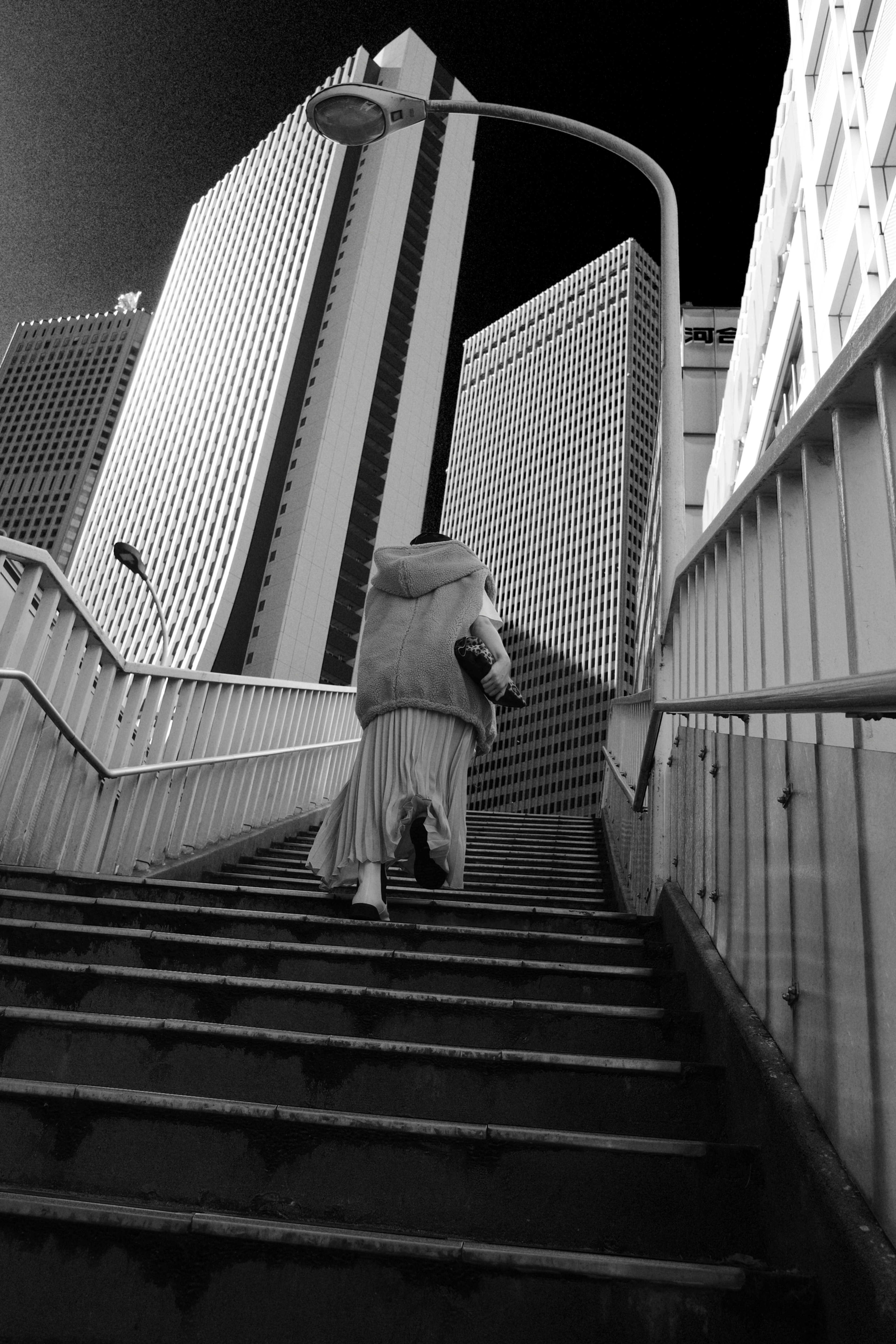 Paisaje urbano en blanco y negro con un monje subiendo escaleras y rascacielos al fondo