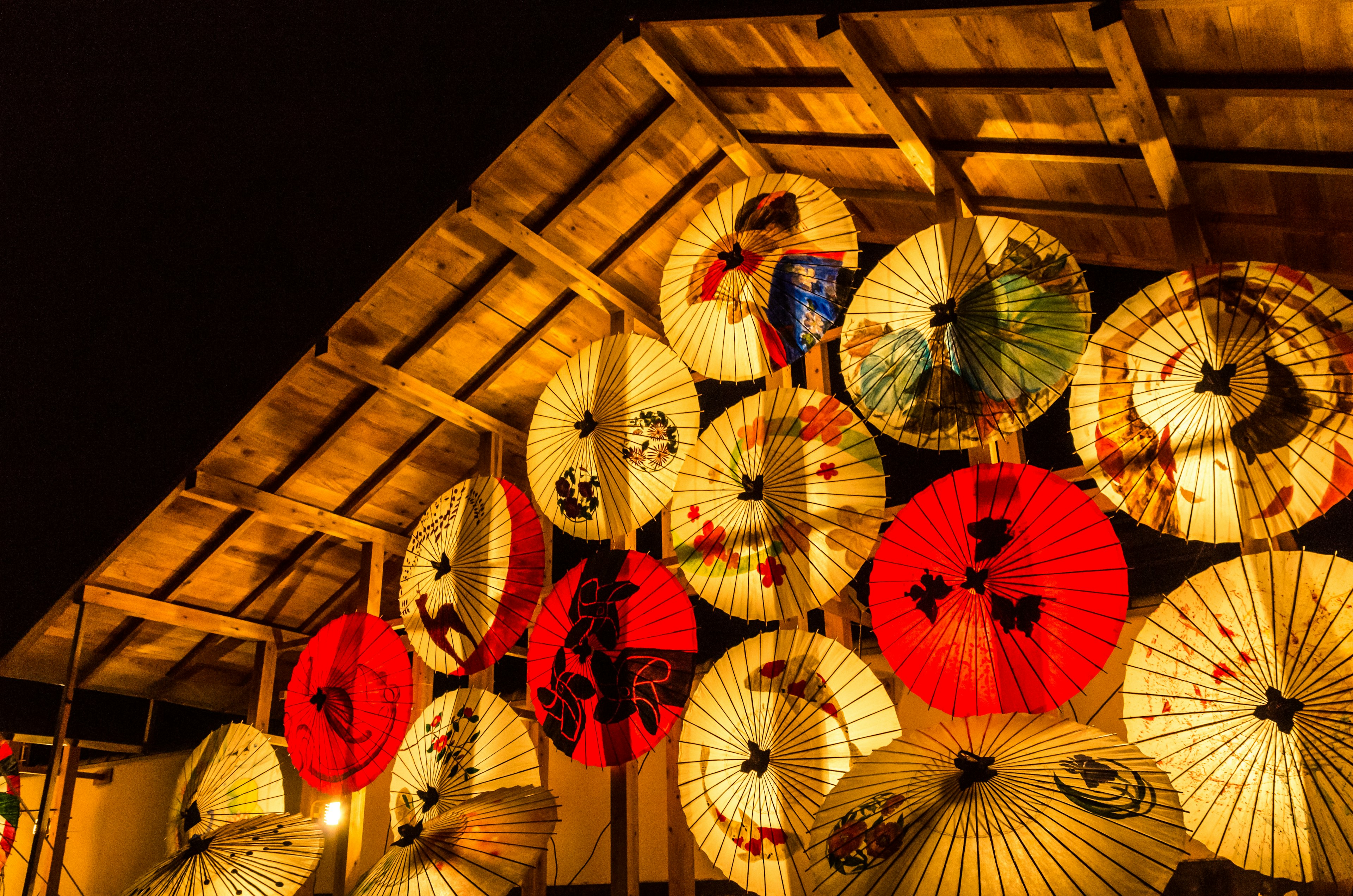 Bunte japanische Regenschirme hängen unter einer beleuchteten Holzstruktur bei Nacht