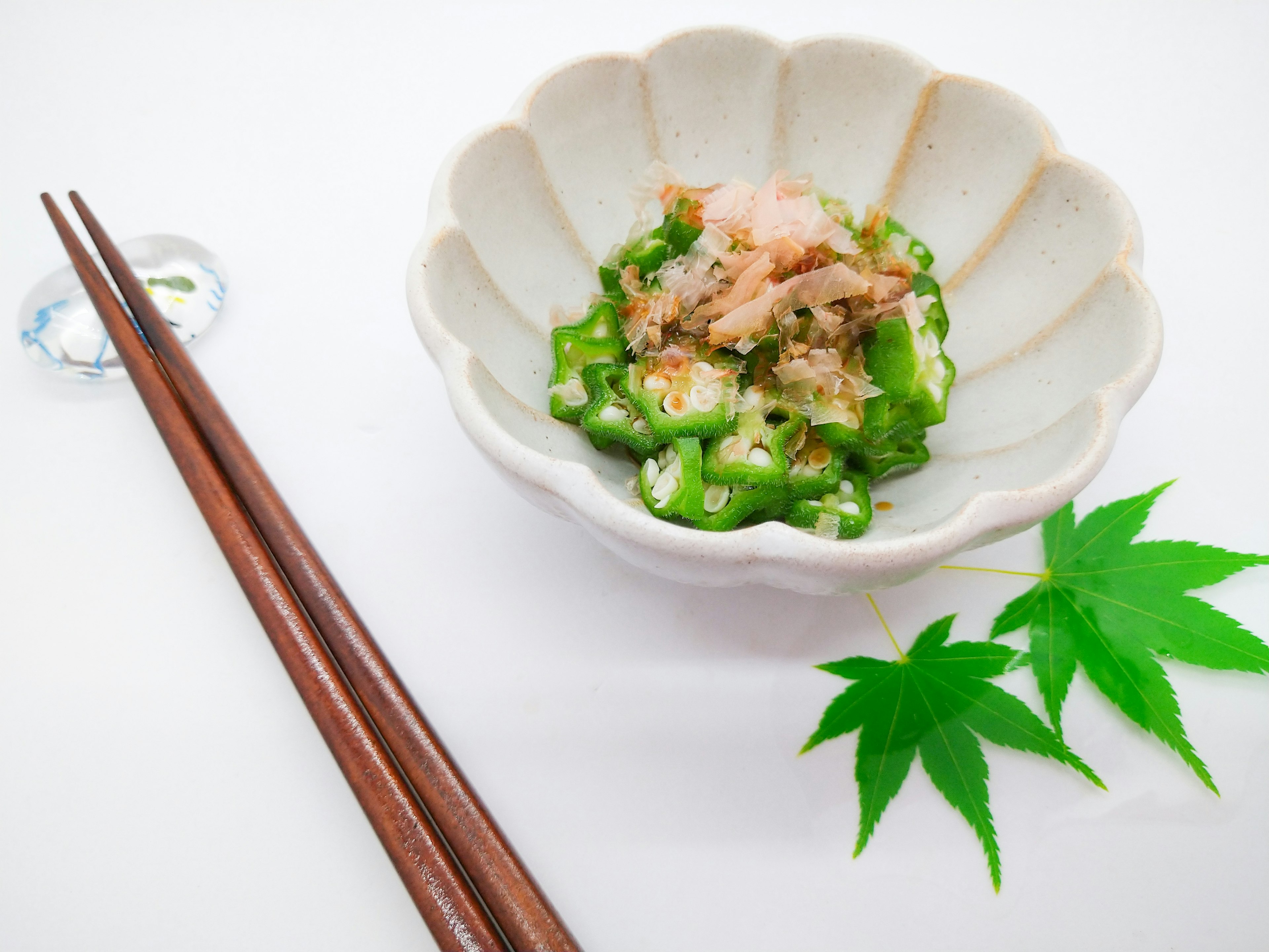 Beautifully arranged Japanese dish with green vegetables and bonito flakes on a white plate