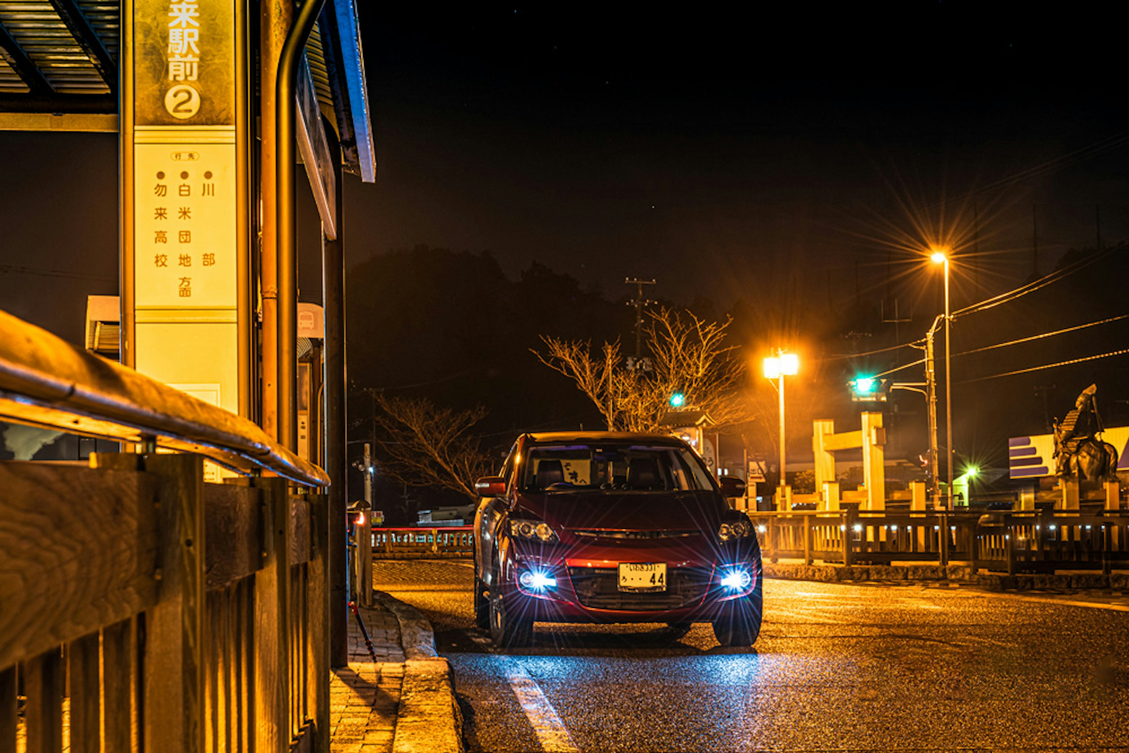 A red car parked at a street corner illuminated by streetlights at night