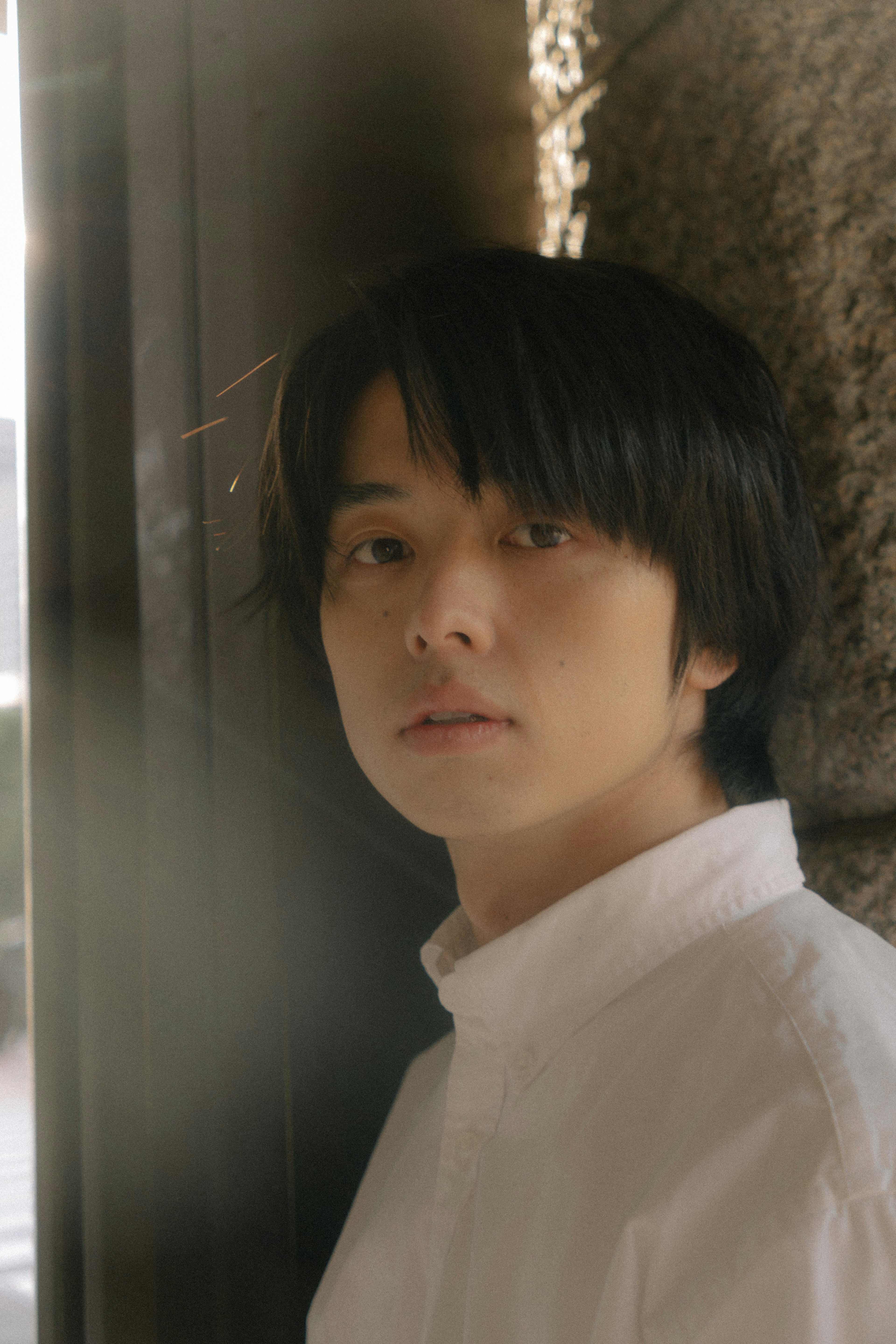 Portrait of a young man leaning against a wall wearing a white shirt soft expression in natural light