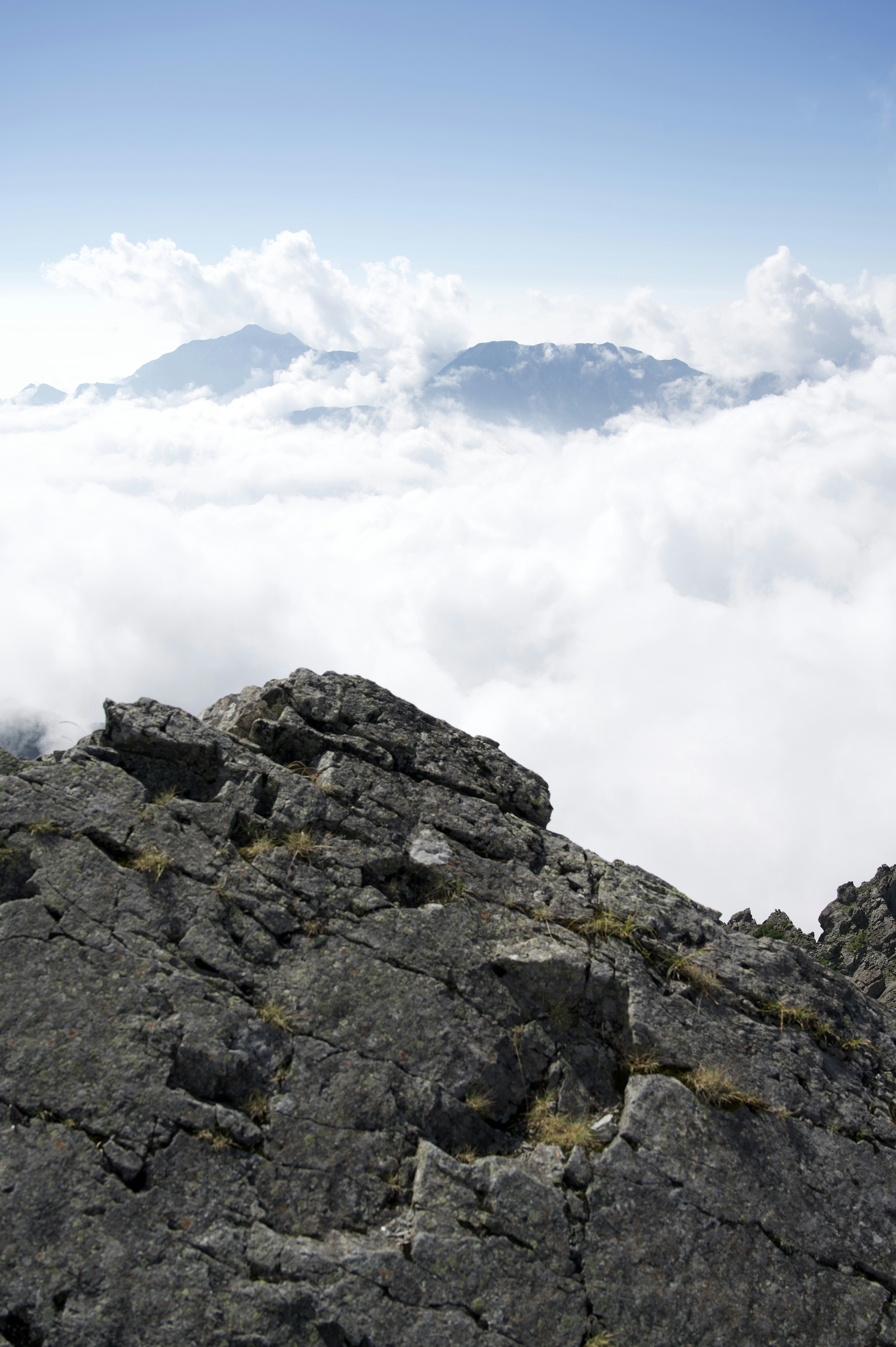 Cime montuose sopra un mare di nuvole con un primo piano roccioso