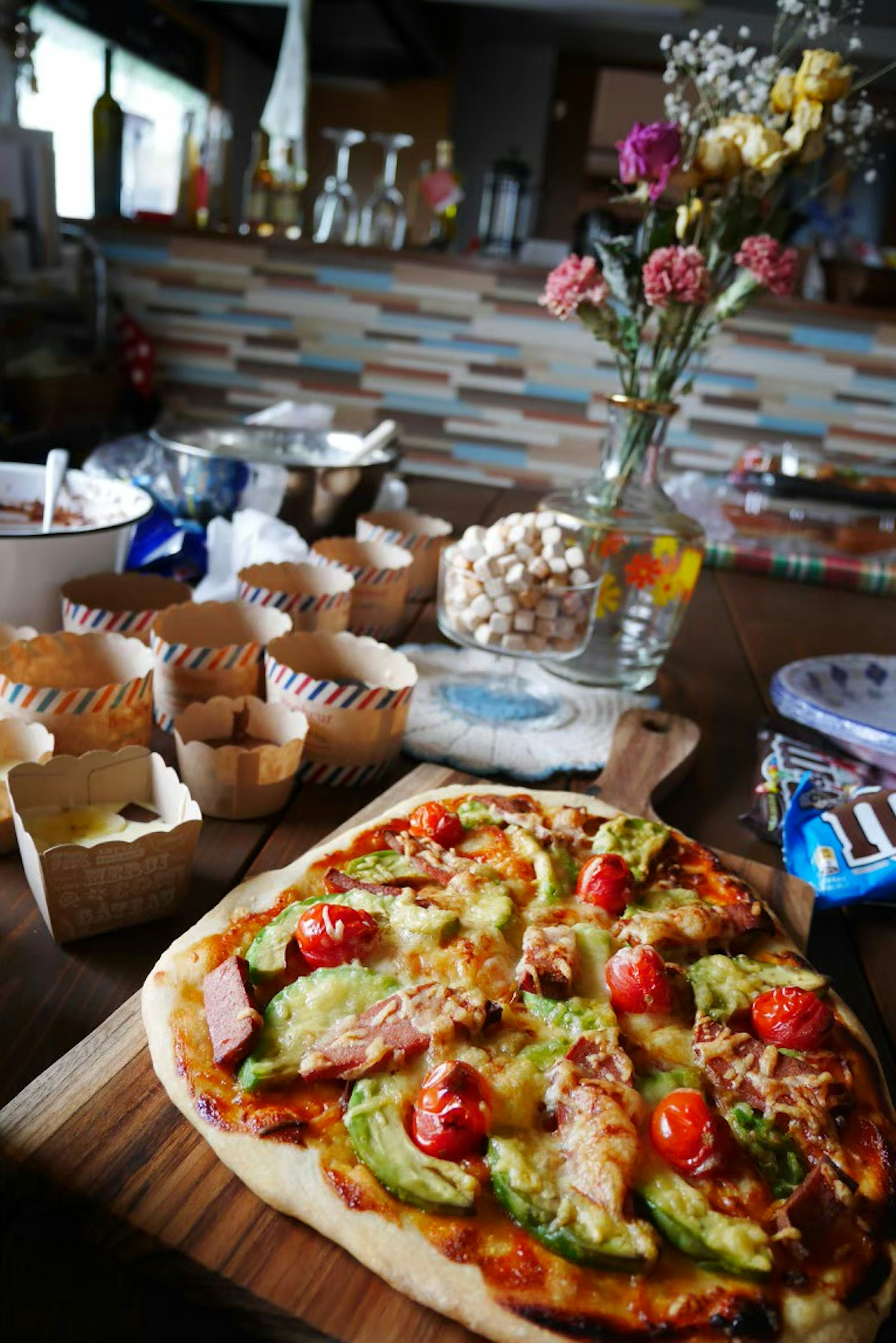 Une pizza garnie de légumes colorés et de tomates à côté d'un vase de fleurs