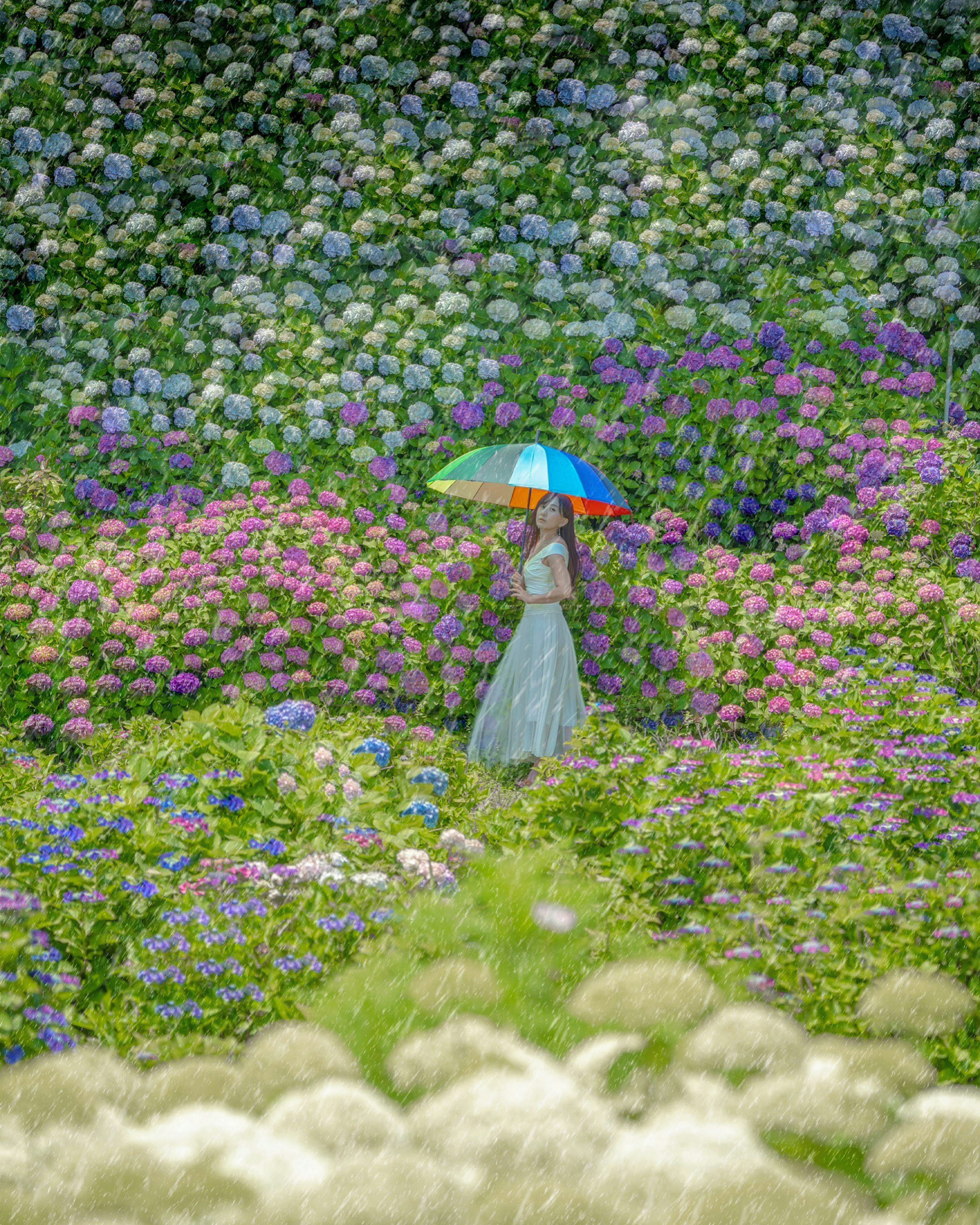 色とりどりの花々に囲まれた女性が傘を持って歩いている風景