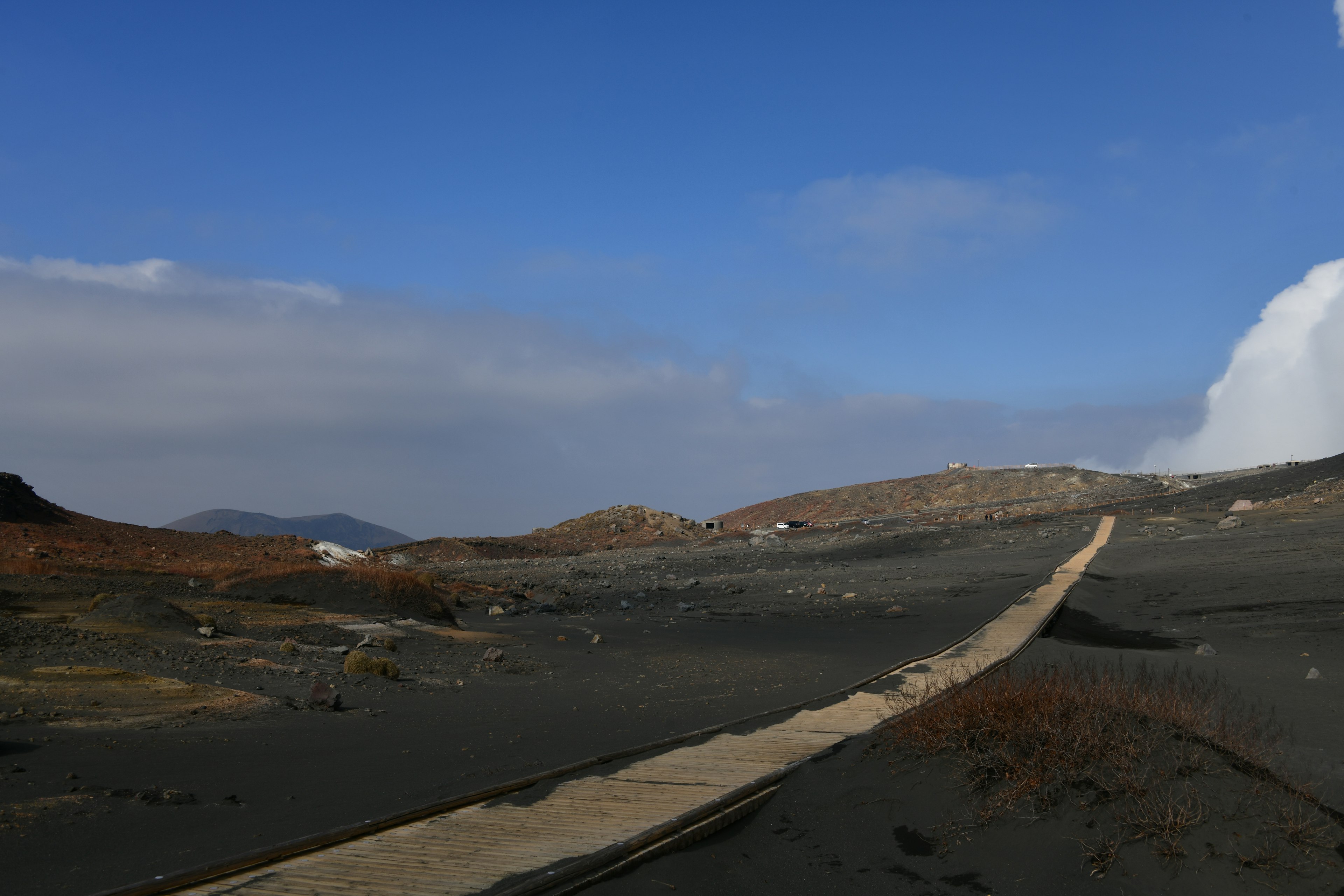 Landschaft mit schwarzem Sand und Holzweg unter blauem Himmel