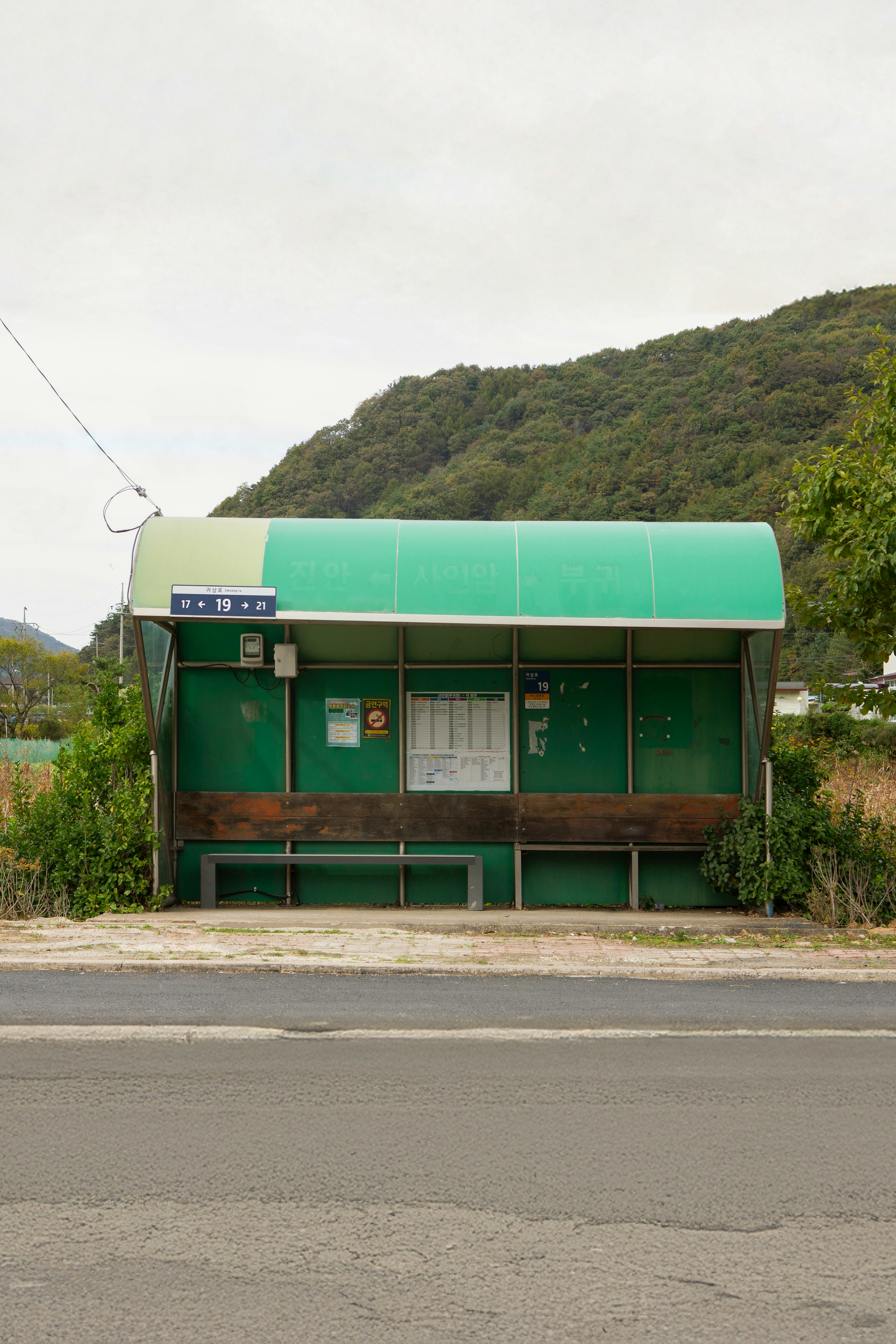 緑のバス停が道路沿いに立っている背景には山が見える