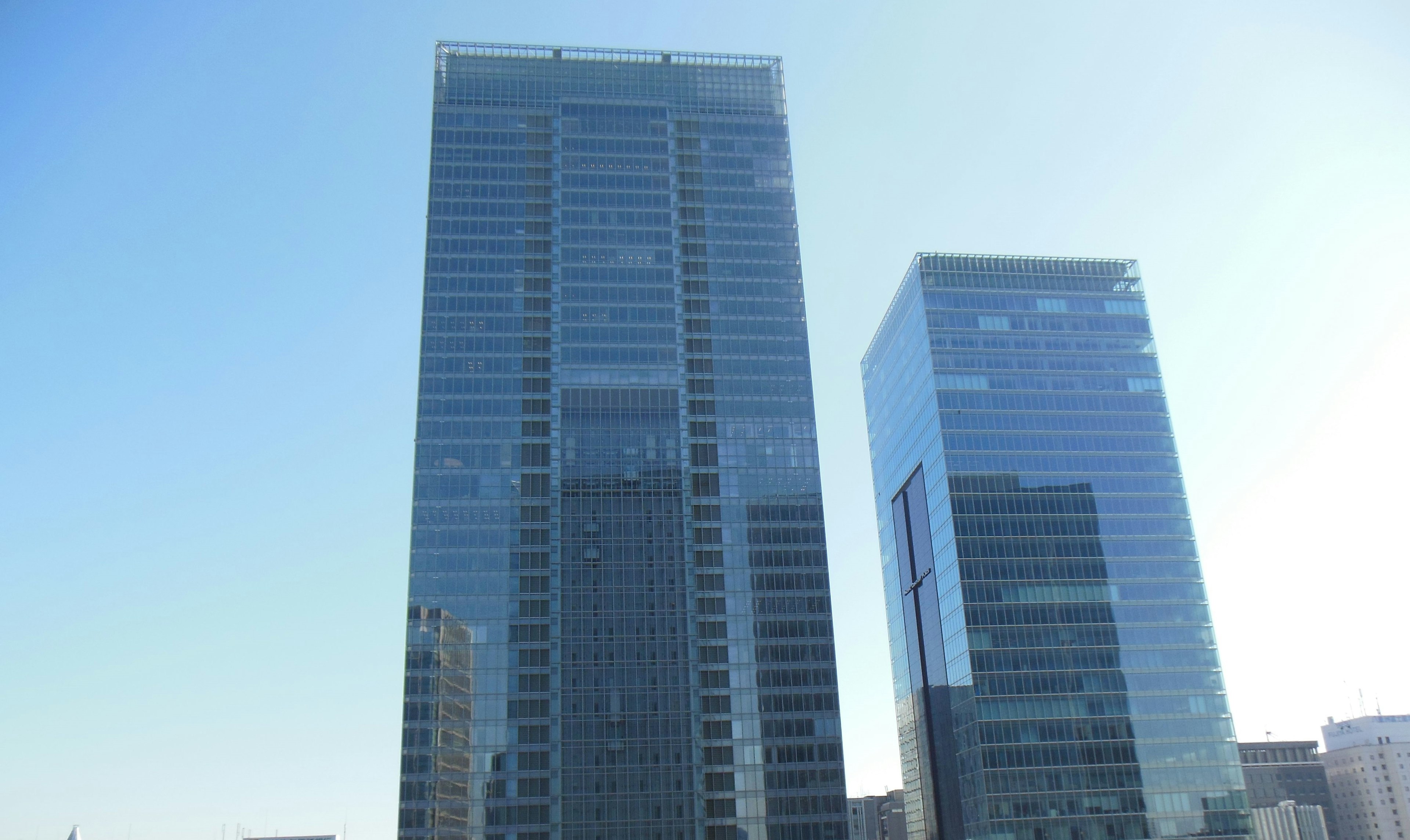 Dua gedung pencakar langit modern yang memantulkan langit biru