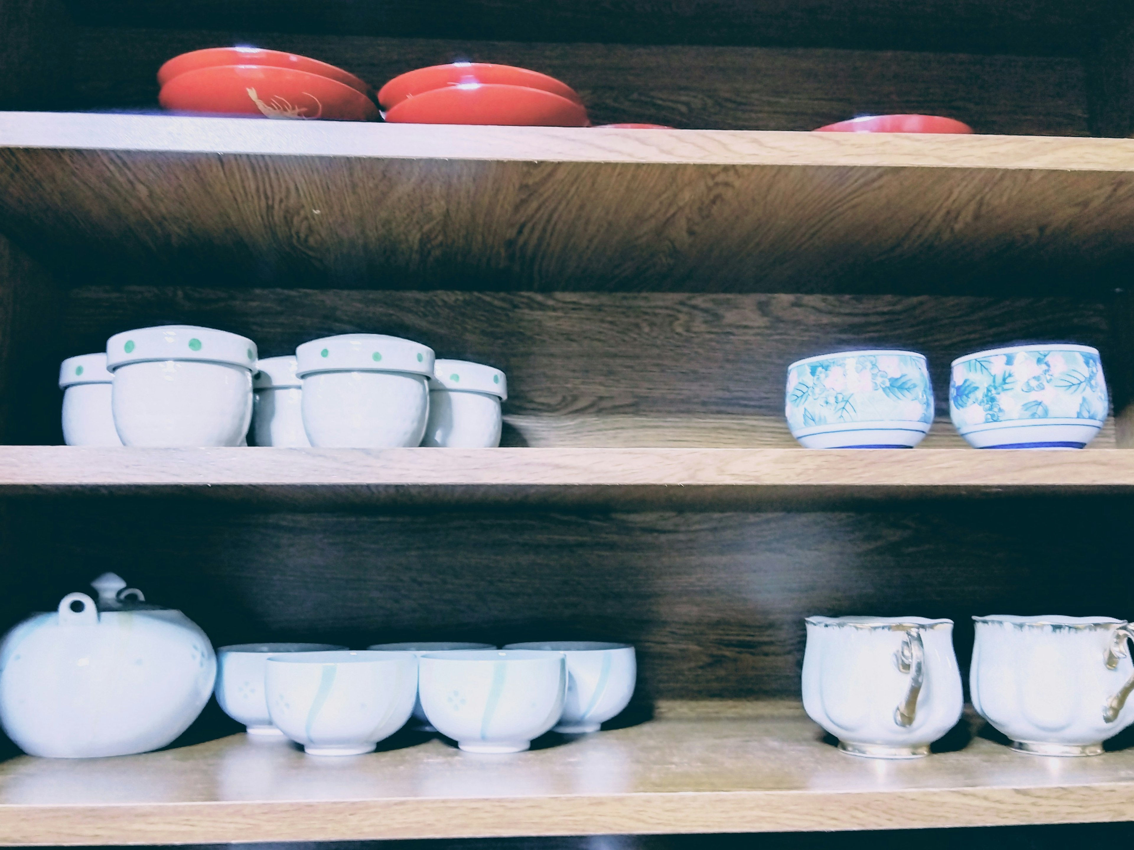 Ceramic dishes and red plates arranged on a wooden shelf