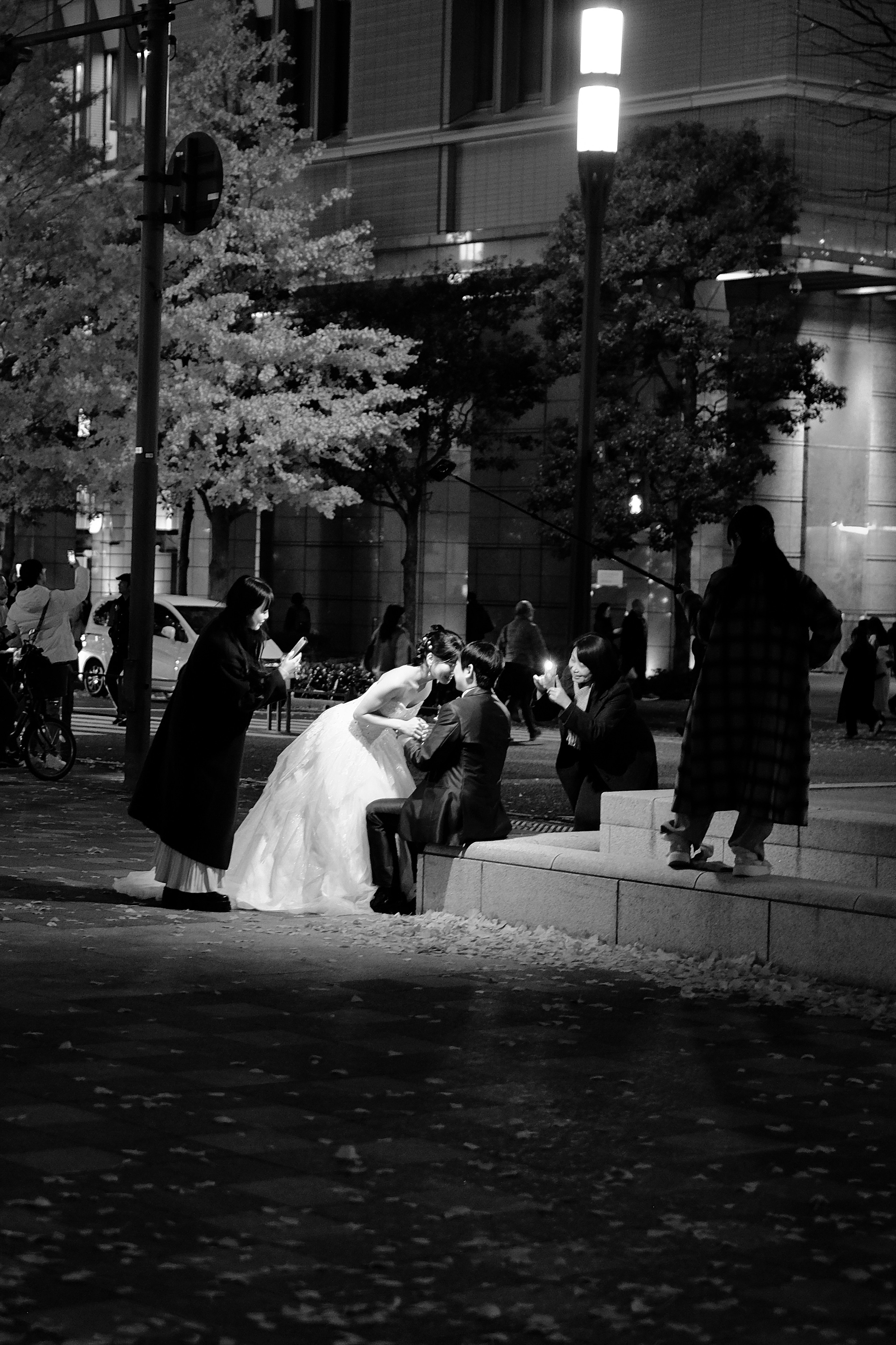 Couple in wedding attire embracing in a park at night with onlookers