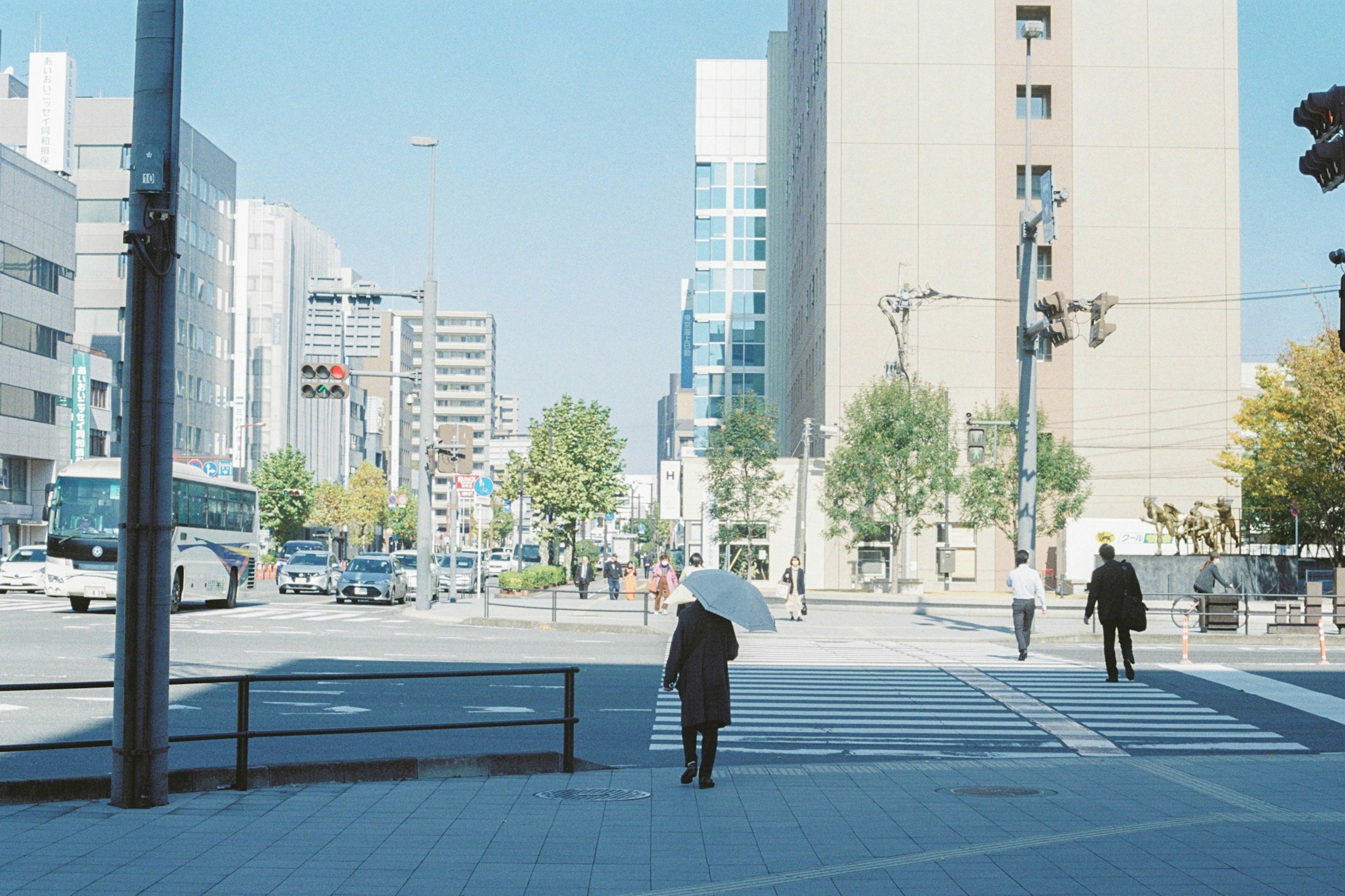 Una mujer caminando con un paraguas bajo un cielo azul junto a edificios modernos