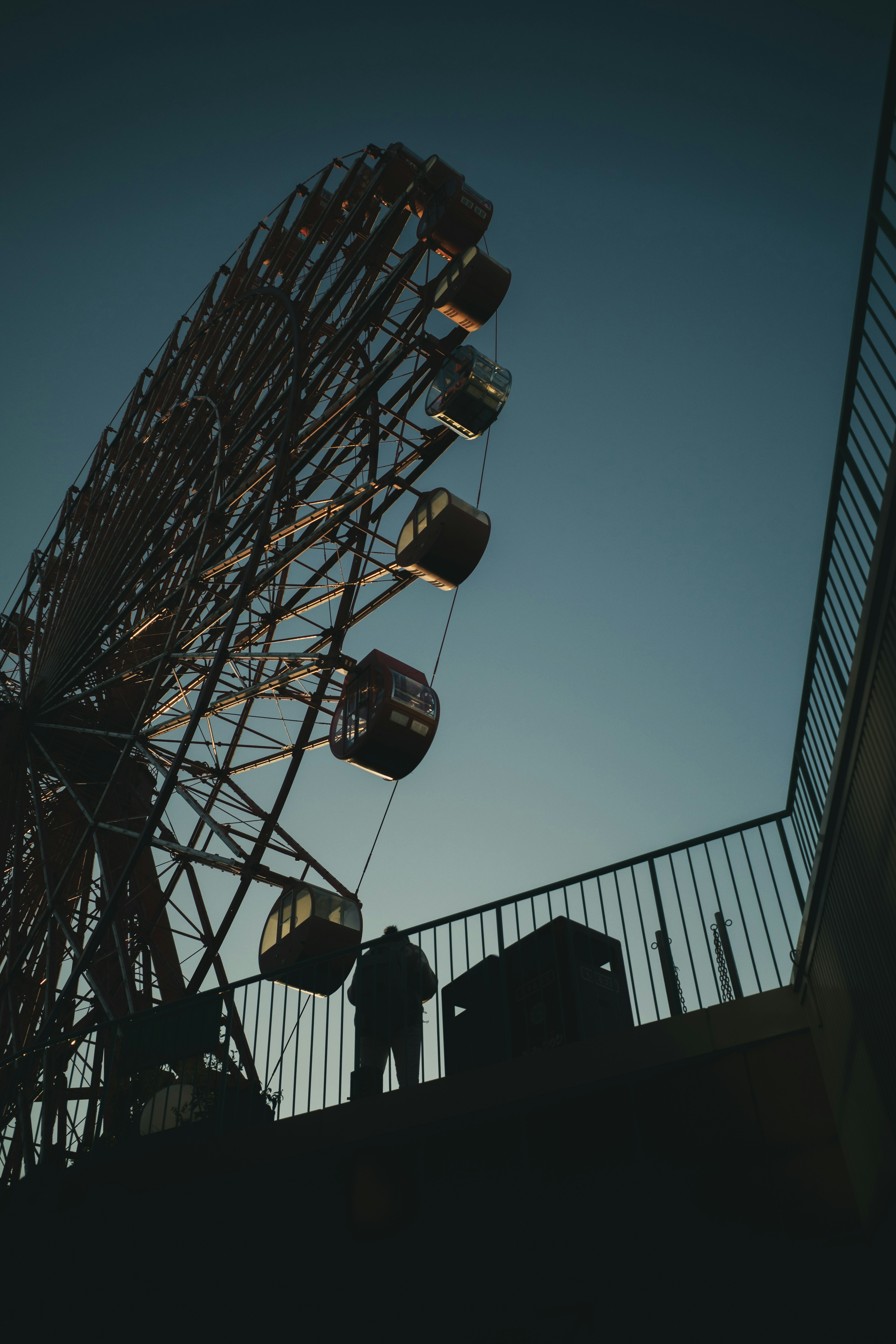 Siluet roda ferris dan sosok di latar belakang langit senja