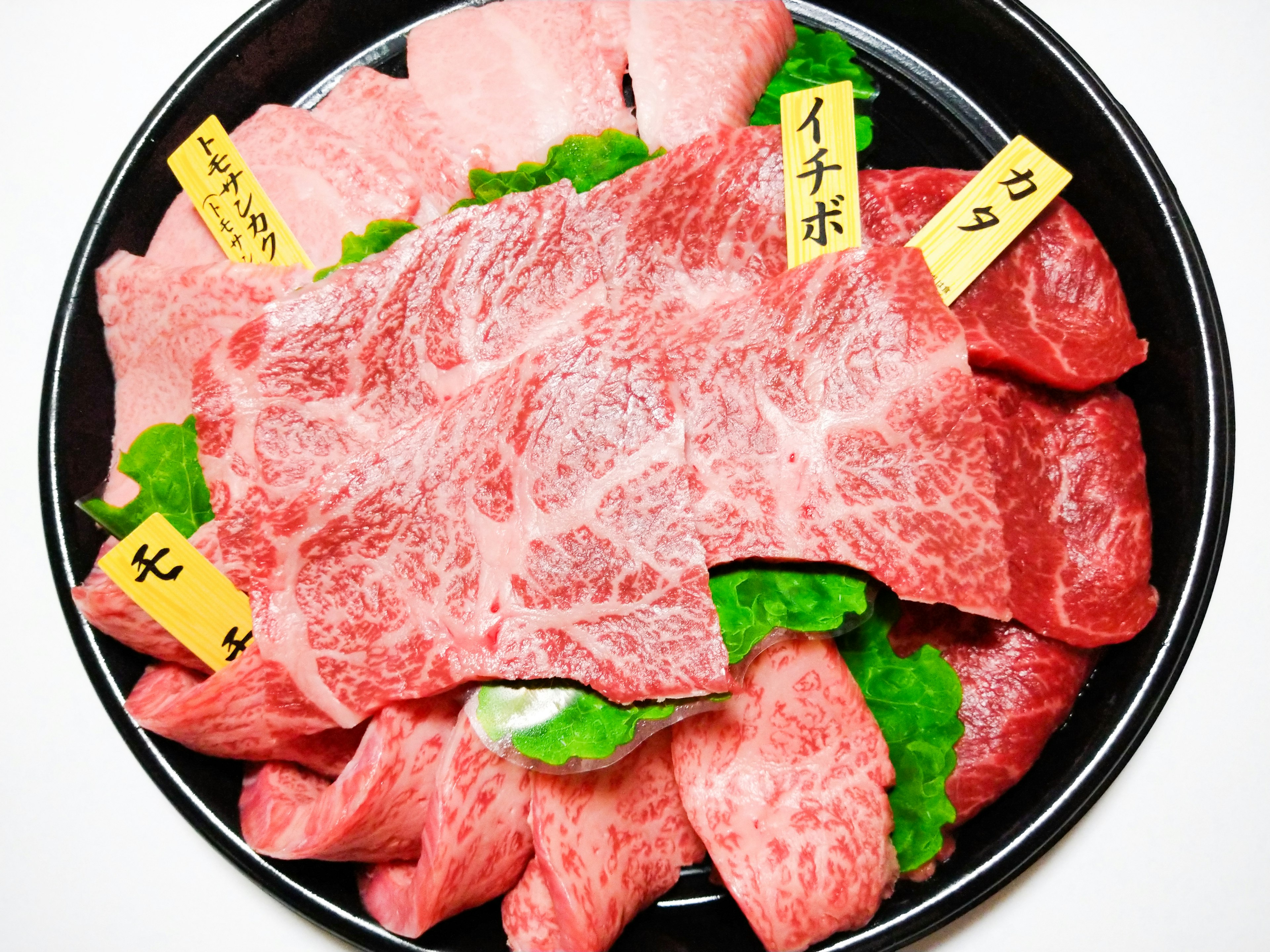 A platter of assorted marbled meats garnished with lettuce and labeled cuts