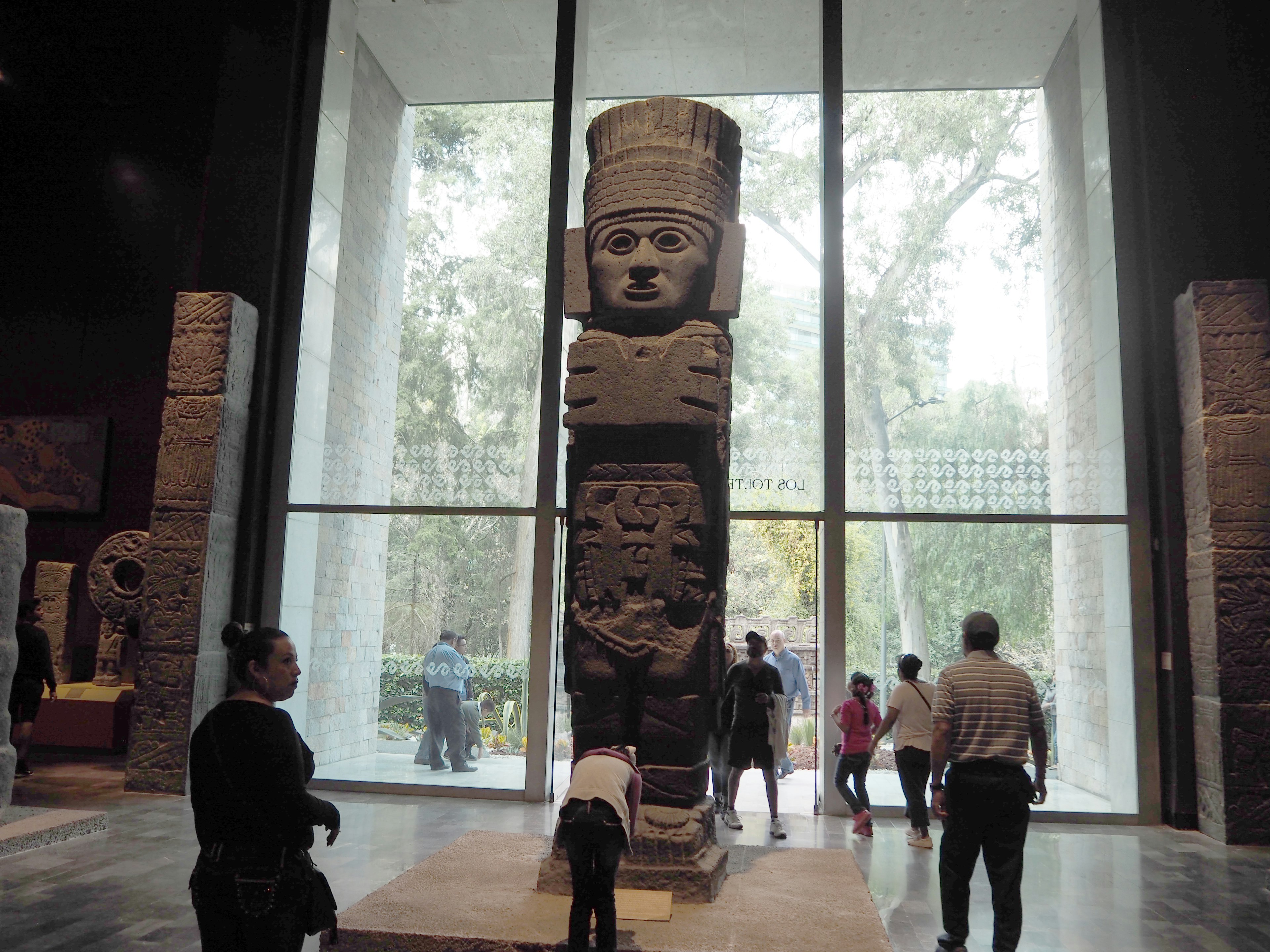 Grande statua di pietra esposta in un interno di museo persone che camminano intorno