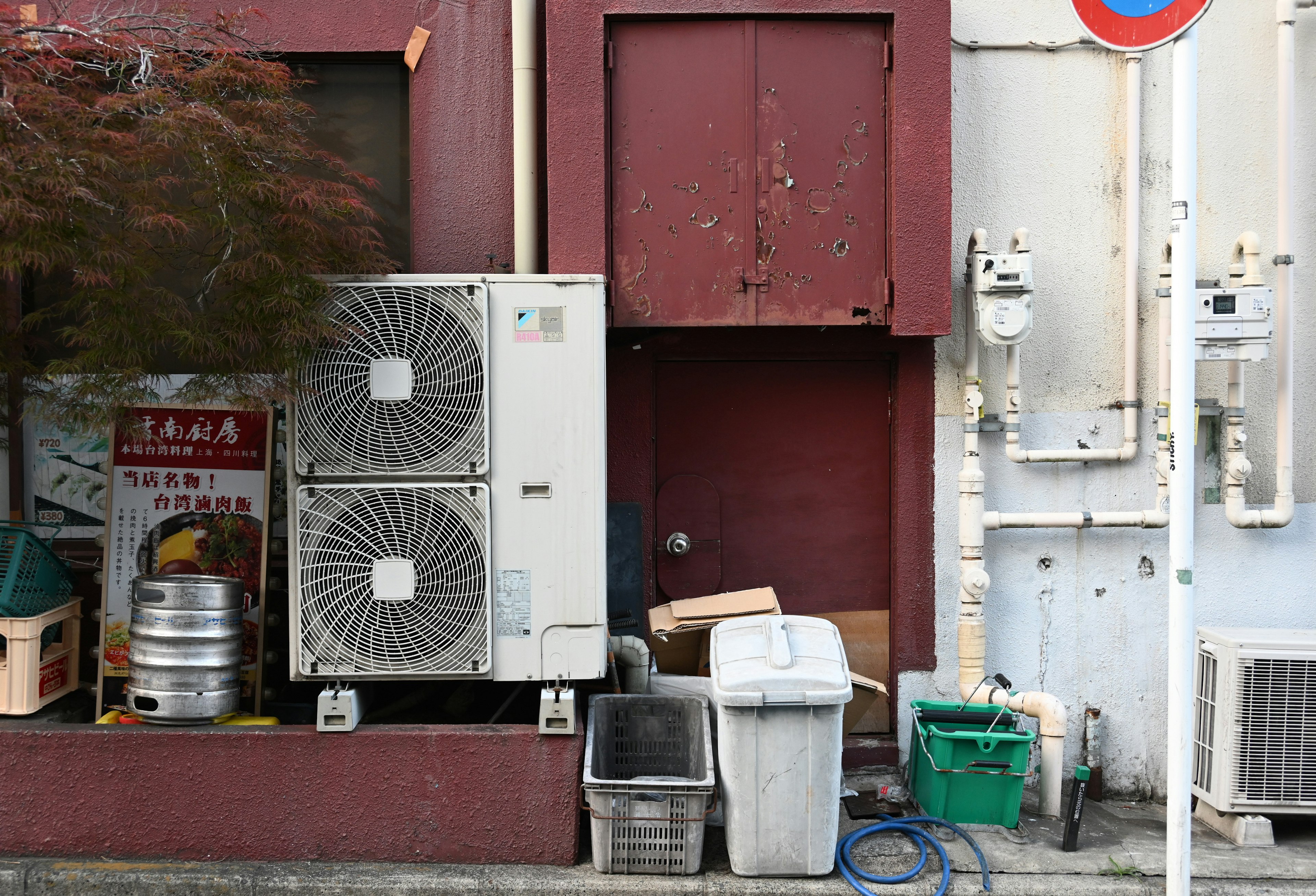 Scene with air conditioning units and trash bins against a red wall