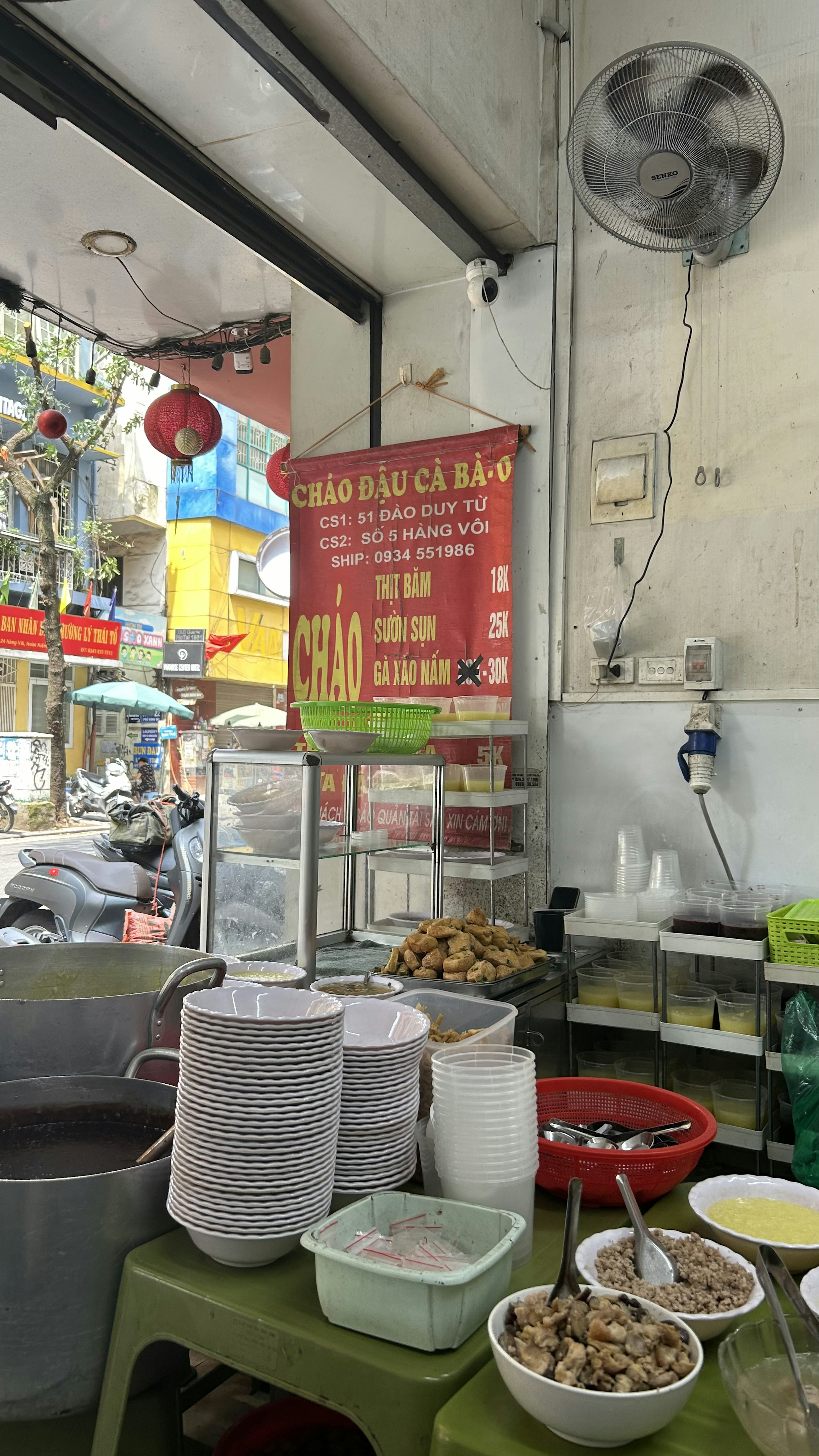 Vista interna di un chiosco di street food vietnamita con ciotole impilate e un menu esposto