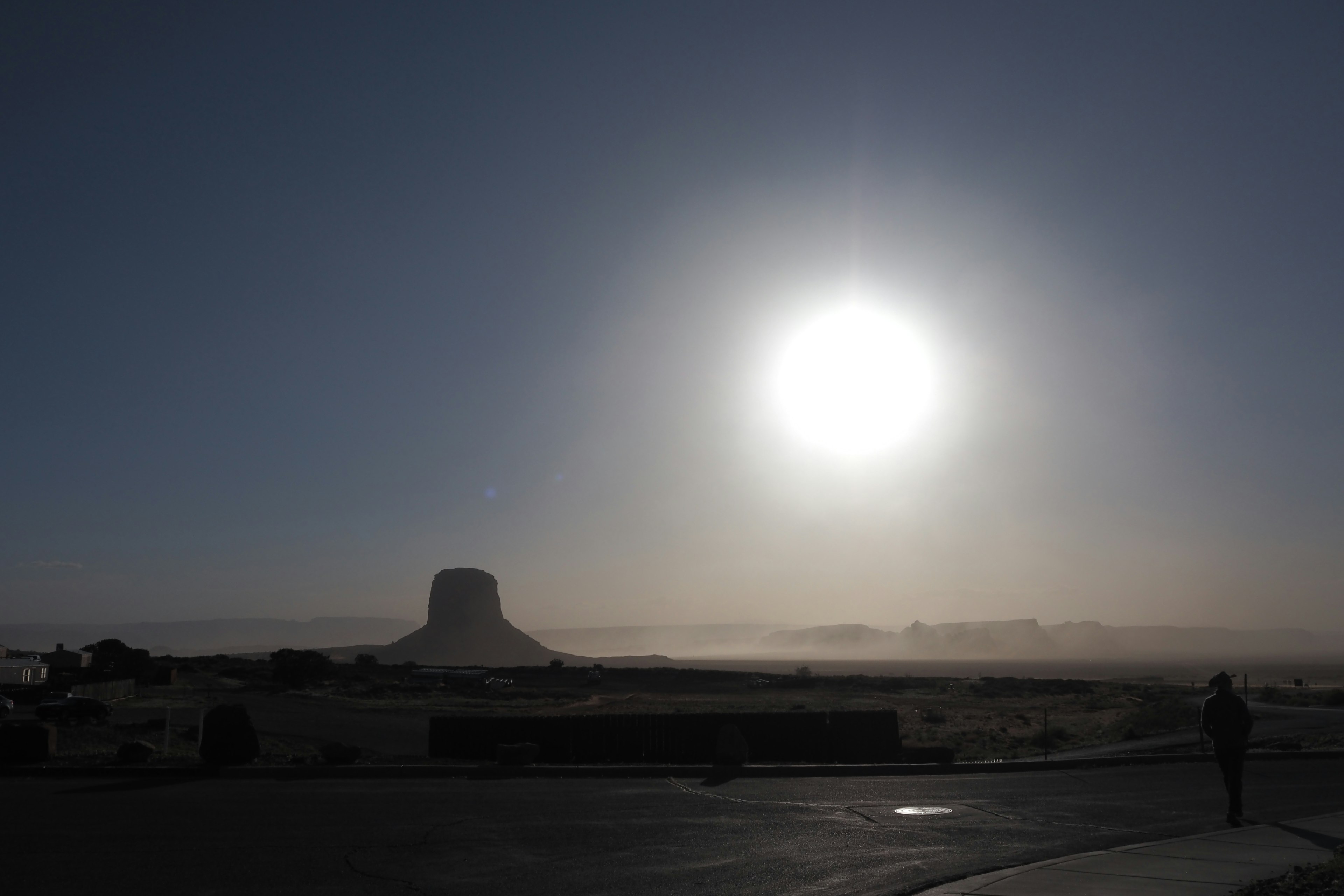 Un gran sol brilla en el cielo con niebla alrededor de un edificio distintivo a lo lejos