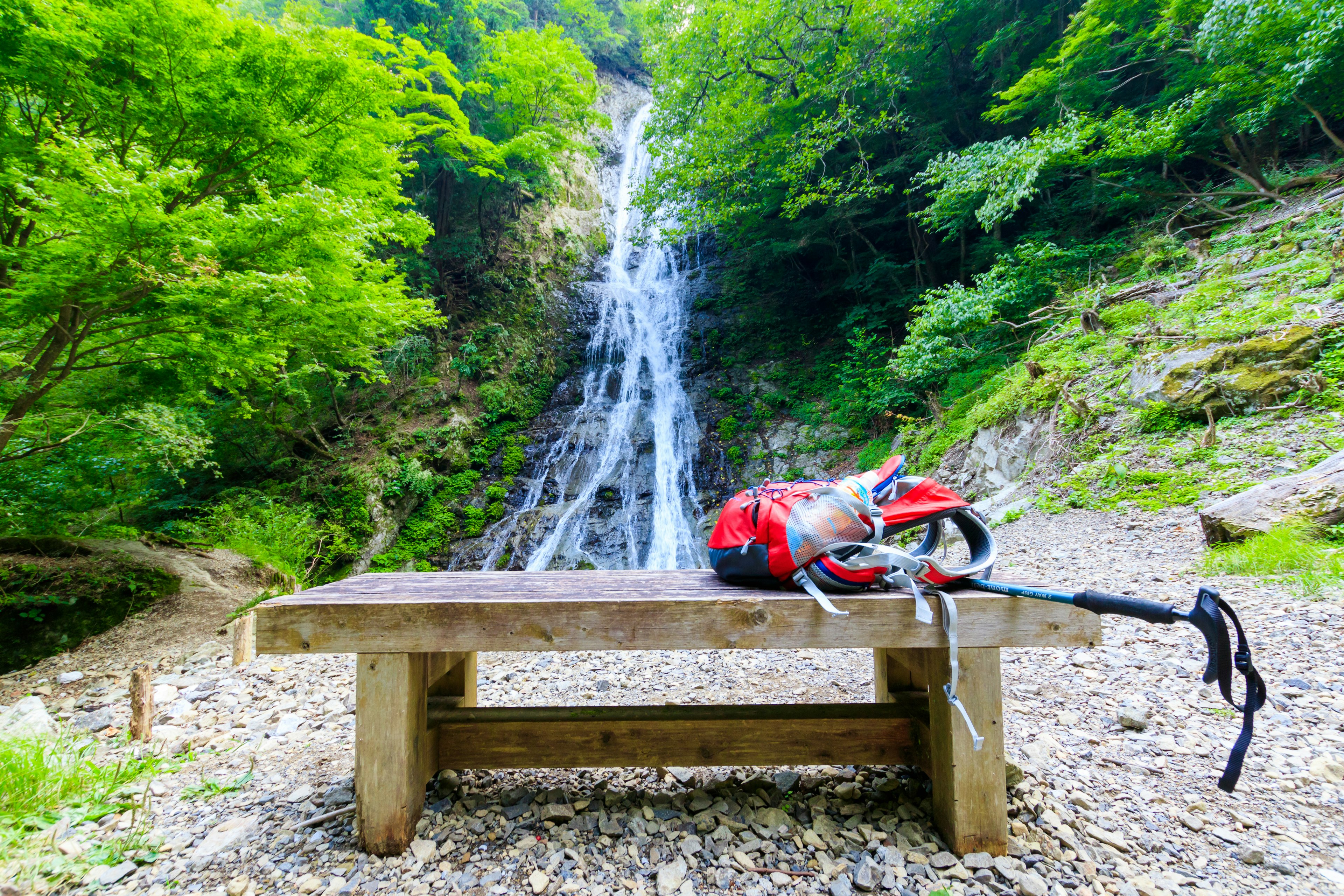 Wooden bench with a red backpack in front of a waterfall