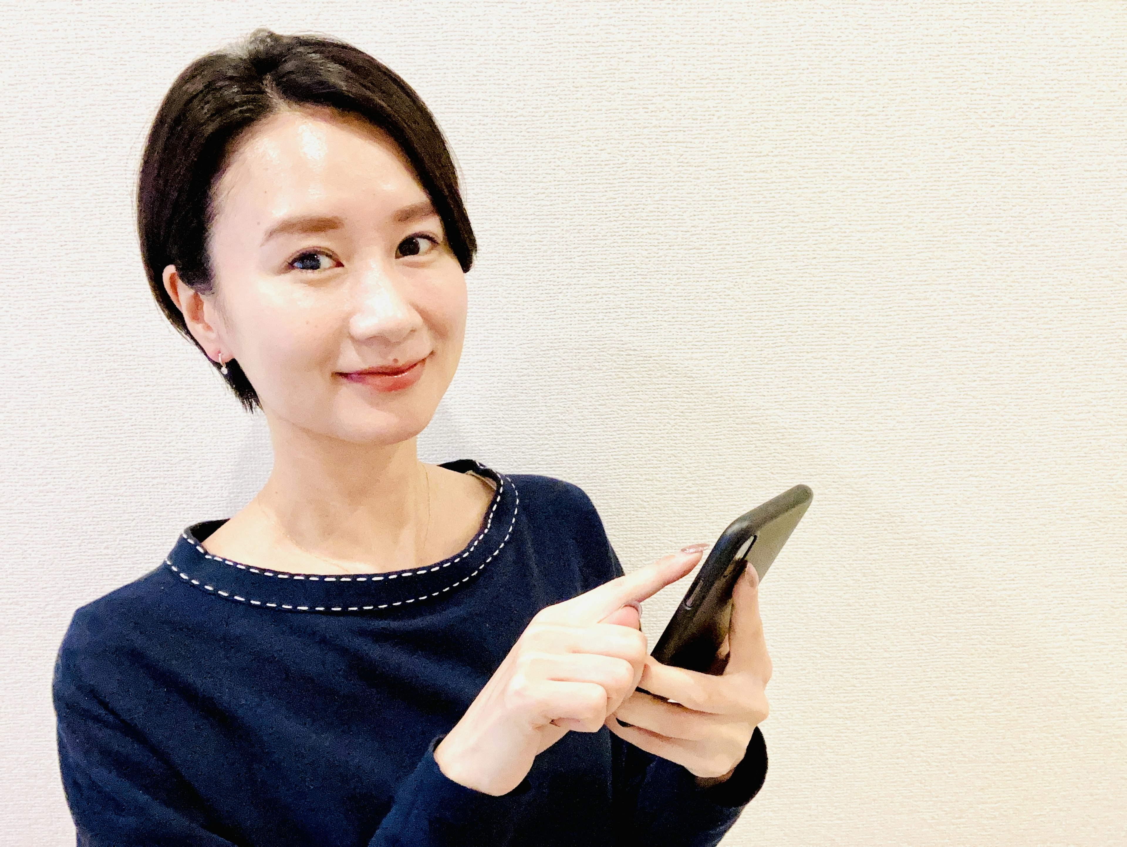 スマートフォンを持って微笑む女性が白い背景に立っている