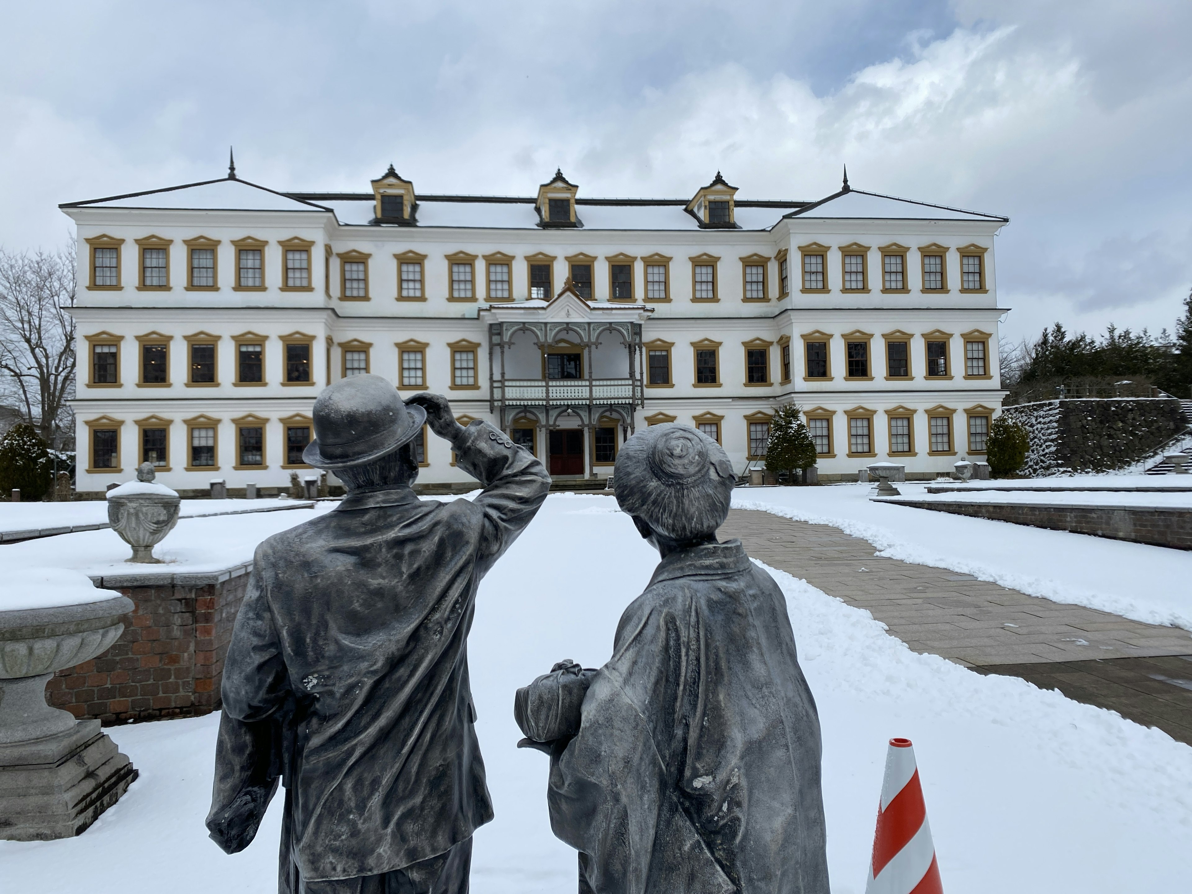 Bronzestatuen eines Paares, das ein großes Gebäude in einem schneebedeckten Garten betrachtet